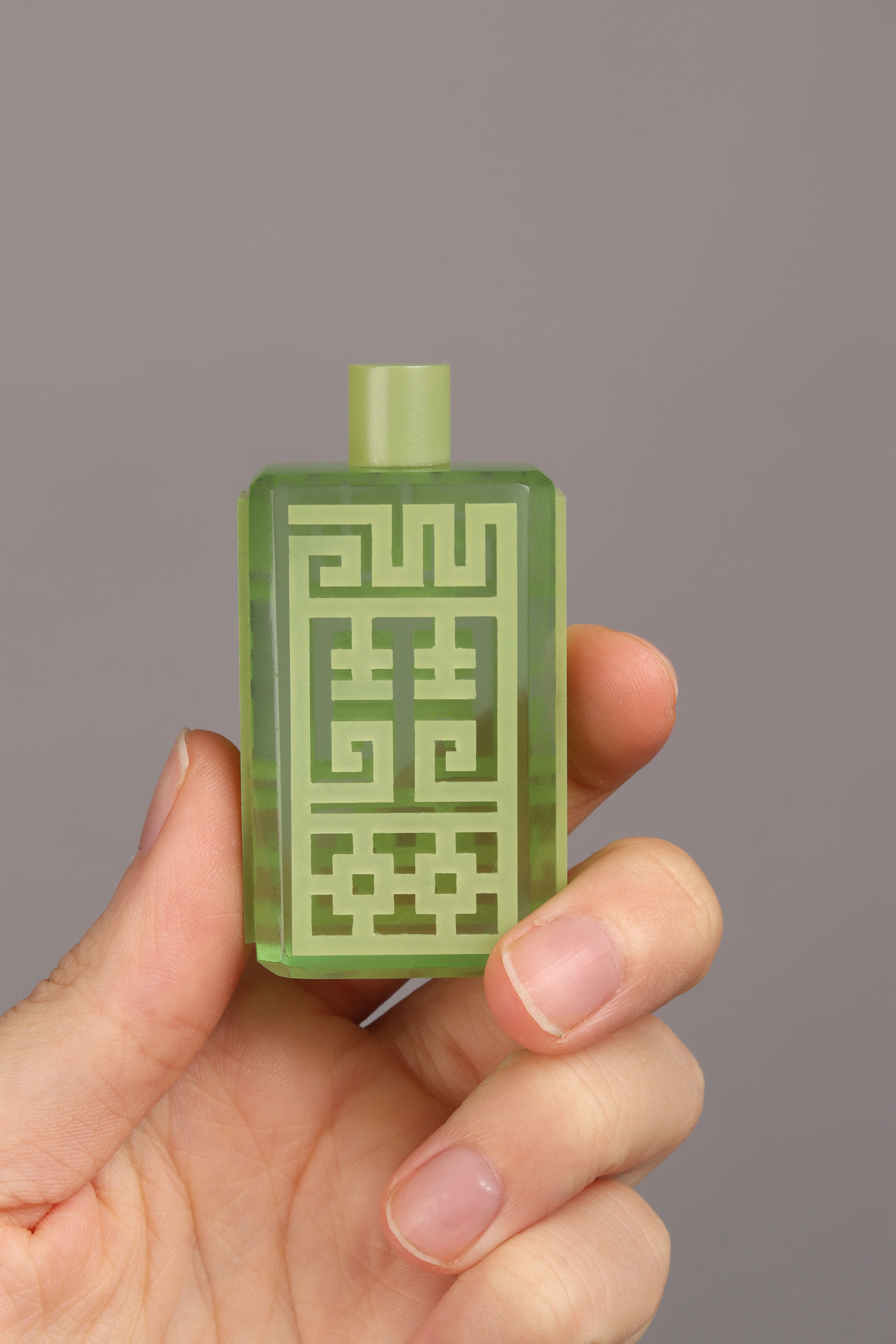 Translucent green perfume bottle with a maze-like design.