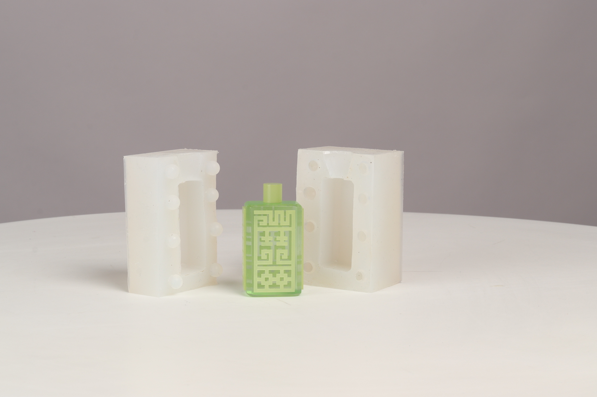 A small green model of a potion bottle with an ornate pattern on the front, standing between two halves of a resin mould.