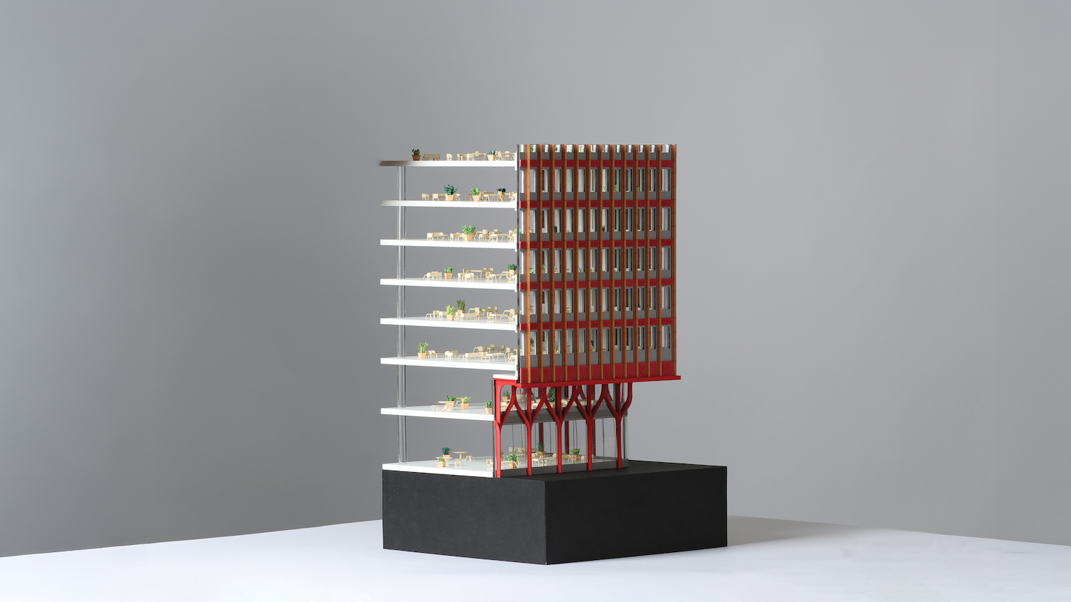 Architectural model with white horizontal platforms and red vertical grid structure on black base against grey background.