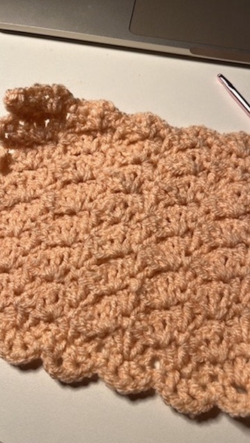 Square of crochet work in brown yarn, viewed on a diagonal lying on a white surface.