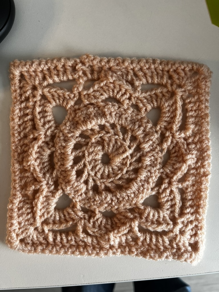Square piece of crochet work in brown yarn with an ornate design on a white surface.