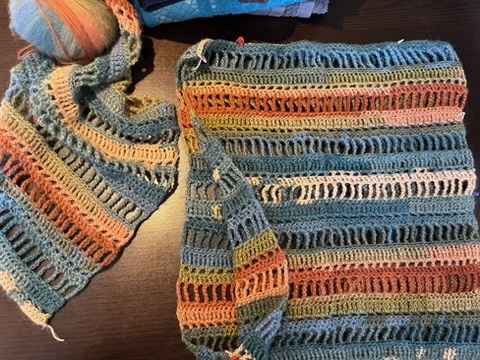 Pieces of crochet work with multi-coloured strips, lying on a dark surface.