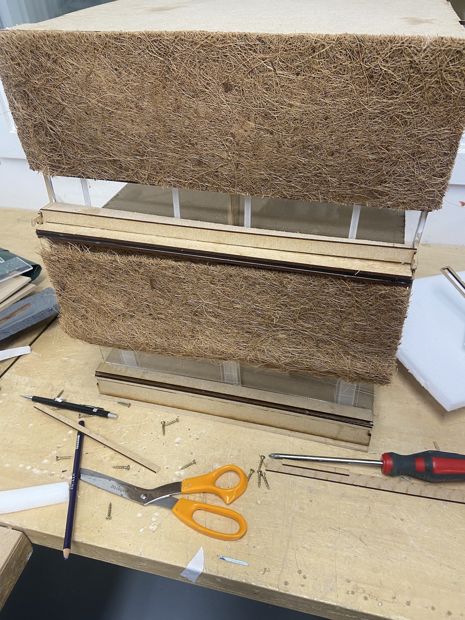 Two samples of thatch on a table top, with tools such as a screwdriver and a pair of scissors lying on the table in front of it.