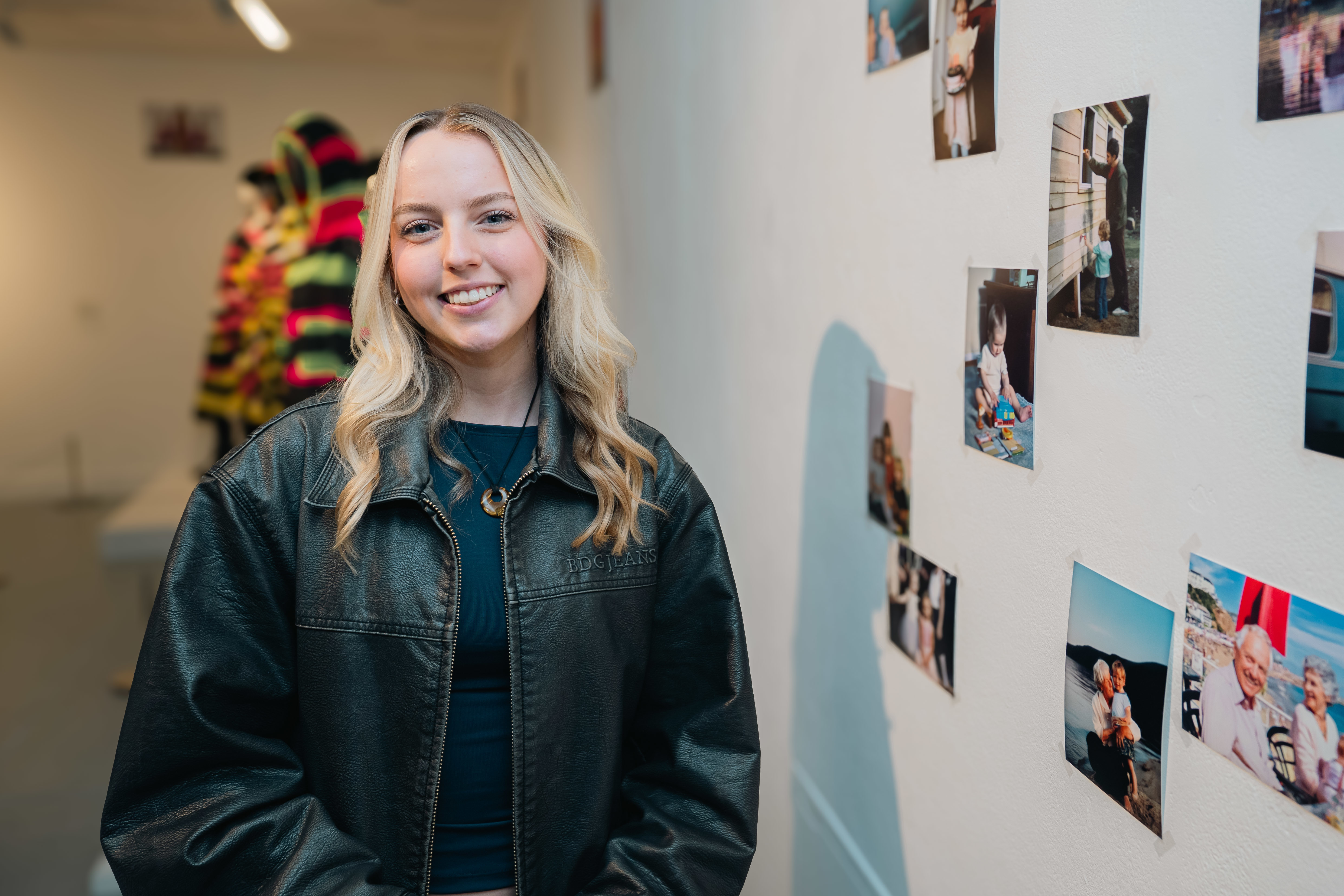 Headshot of J Lowther standing next to some of her photography work at TheGallery, Arts University Bournemouth