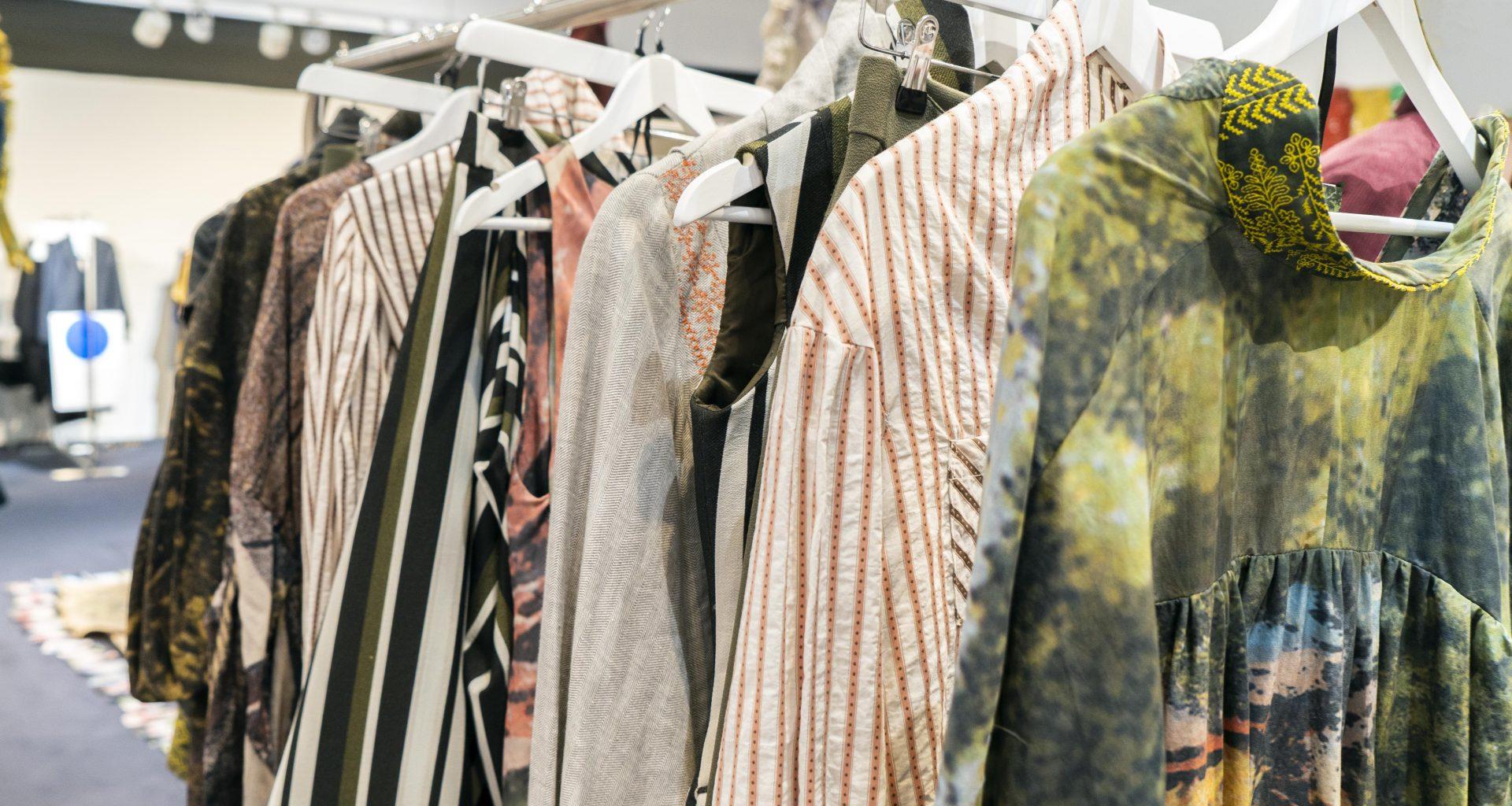 A collection of different shirts hang on hangers backstage at a fashion show