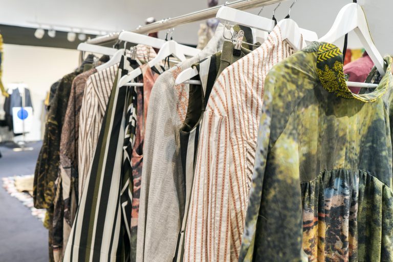 A collection of different shirts hang on hangers backstage at a show at London Fashion Week