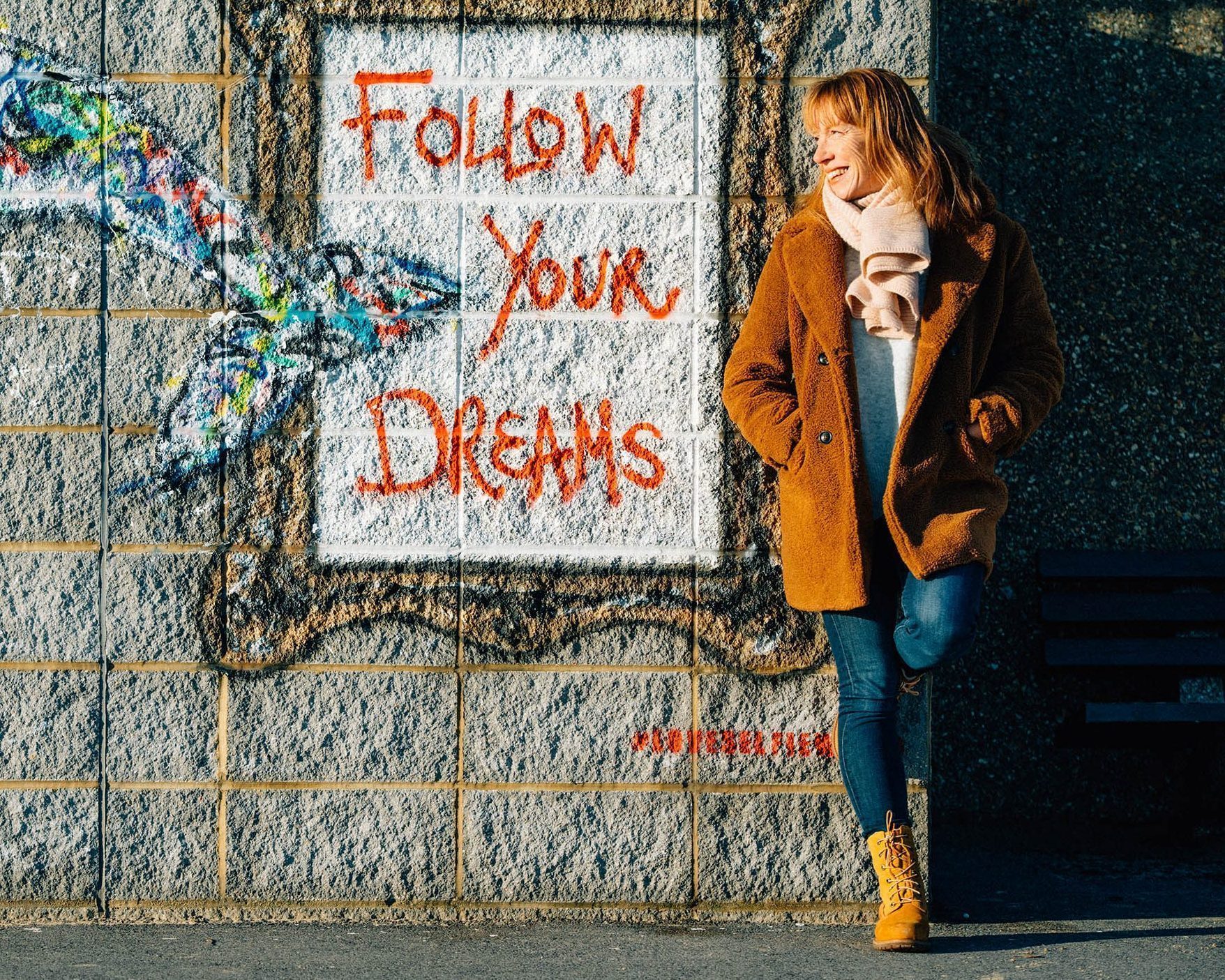 Portrait of J White next to street art with the words "Follow your dreams" in a frame.