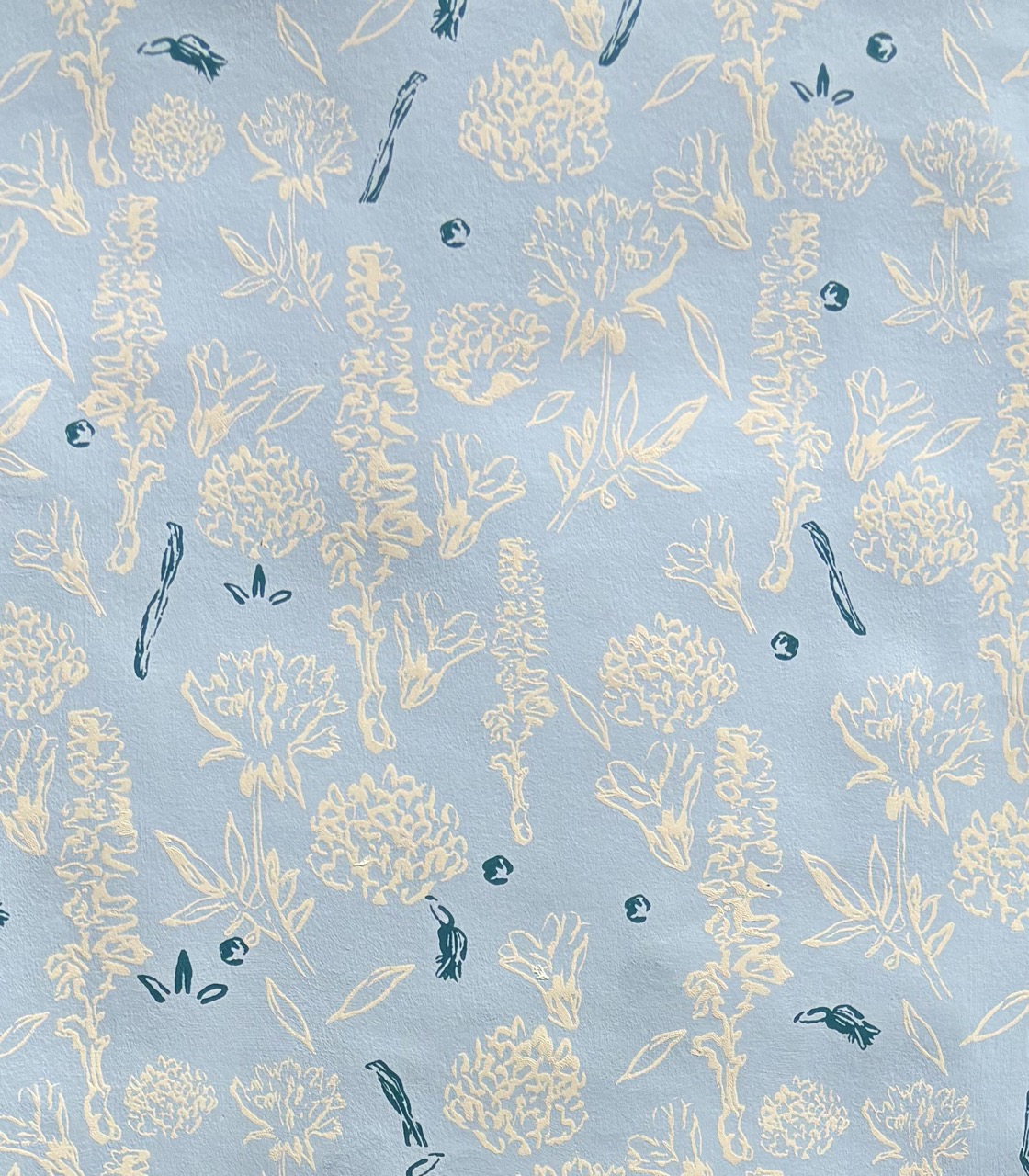A light blue fabric featuring a repeated pattern of delicate flowers and leaves in cream and green. The floral designs are scattered evenly across the surface, creating a soft, botanical aesthetic.