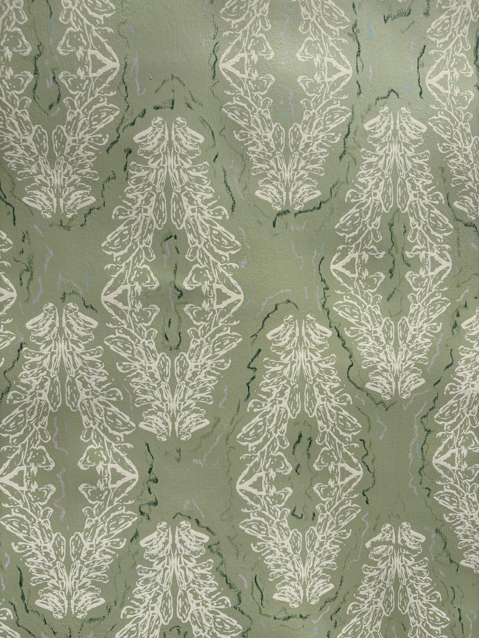 A textured fabric featuring a repeating pattern of white floral motifs set against a muted green background. The design includes intricate details and light shading, creating a layered appearance.