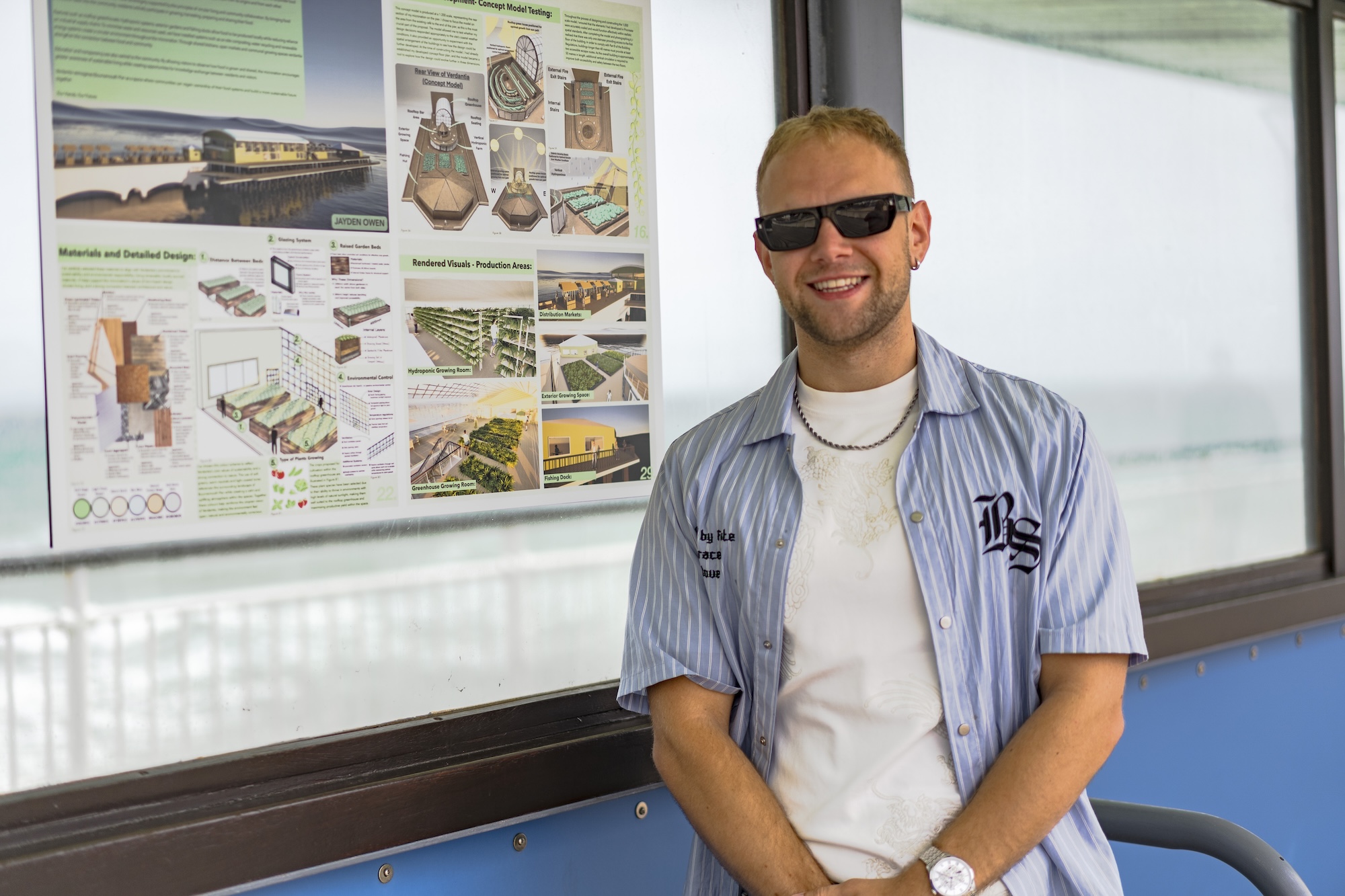 Portrait of J Owen standing next to a poster showing interior and architectural designs and diagrams, on display at Bournemouth Pier.