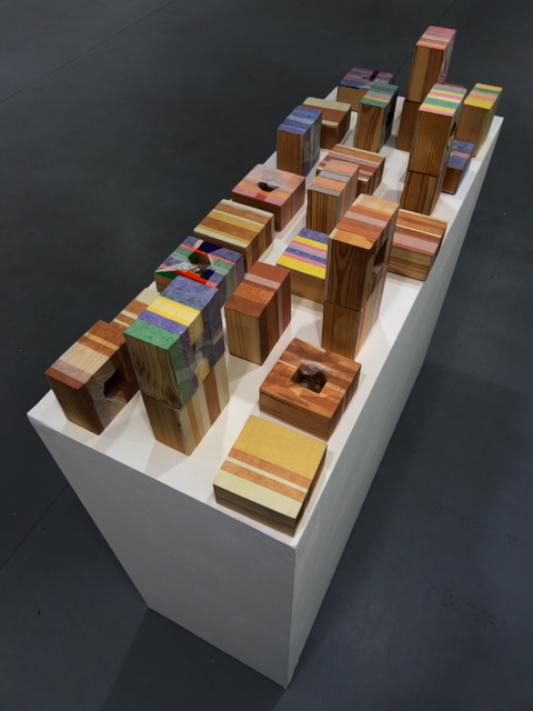 Wooden blocks of varying heights arranged on white rectangular platform, some blocks feature coloured geometric patterns and cutout openings.
