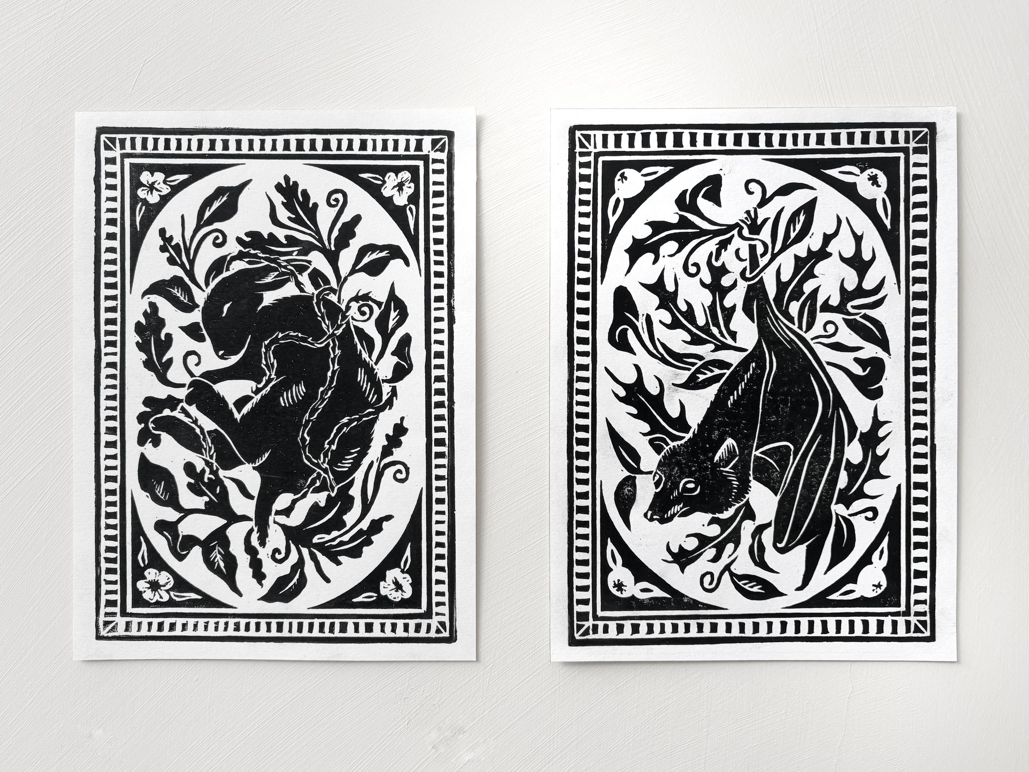 Two bold, black on white prints with ornate borders. One image shows a rabbit, the other shows a bat.