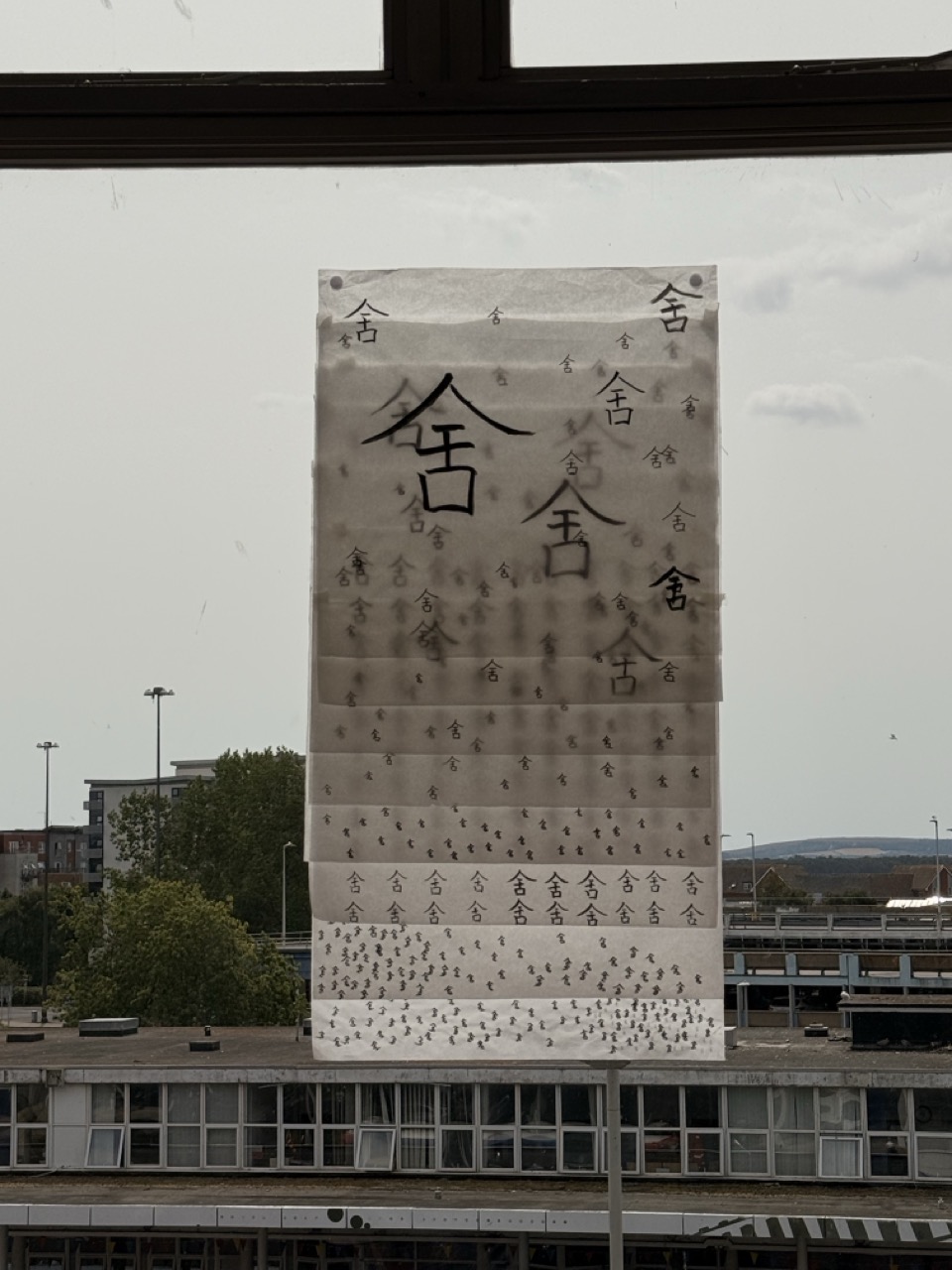 A tall outdoor banner with large Japanese characters stands above a low building, with trees and distant structures in the background.
