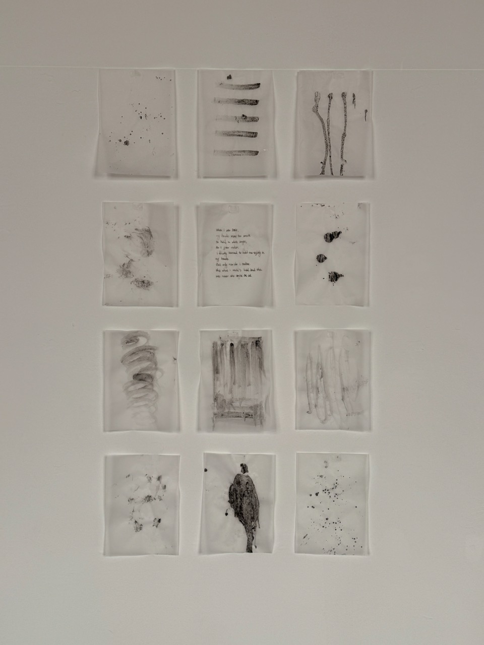 Nine small monochrome abstract drawings are arranged in a three-by-four grid on a pale wall.