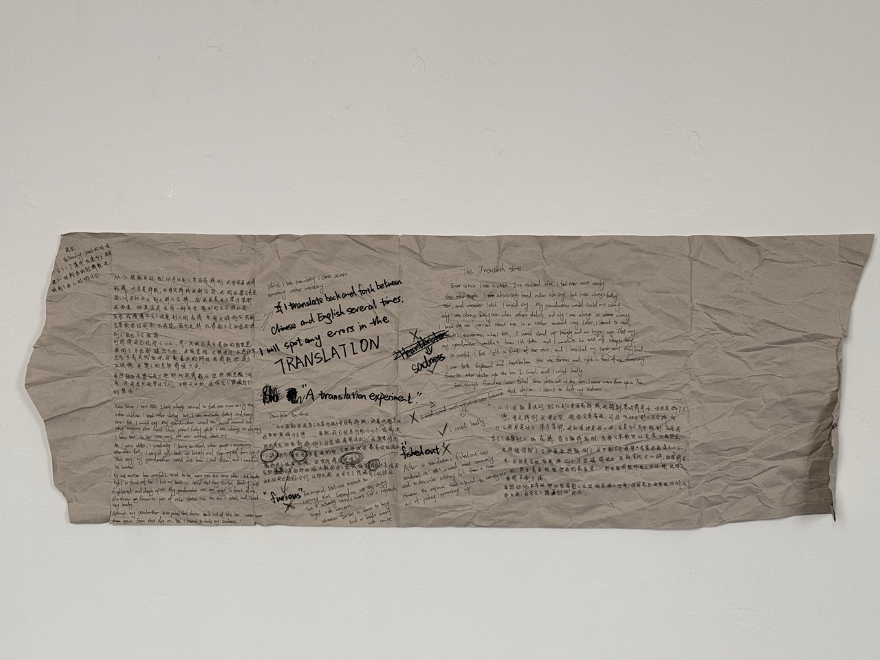 A long crumpled beige sheet with handwritten notes and printed text is taped against a plain white wall.