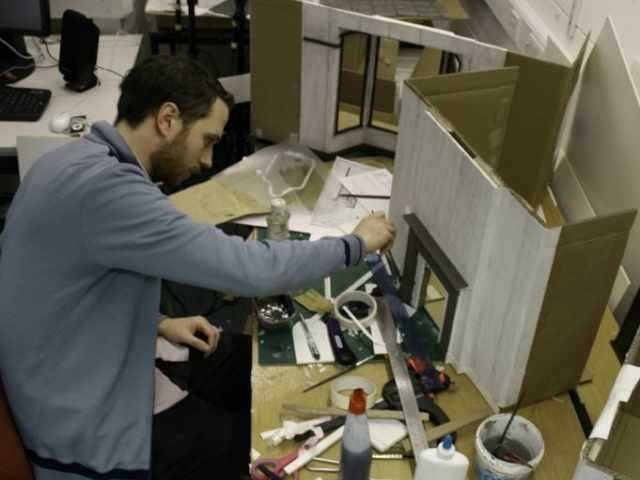 Student working at a table with the model of the front of a building in front of them.