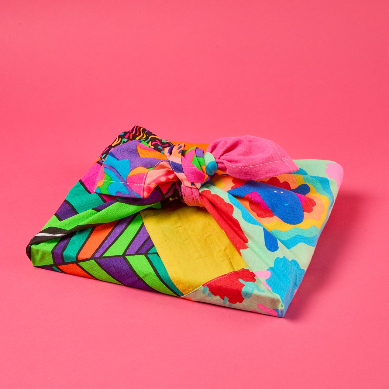 Multicoloured, pattered Lush Knot Wrap on a bright coral pink/red background.