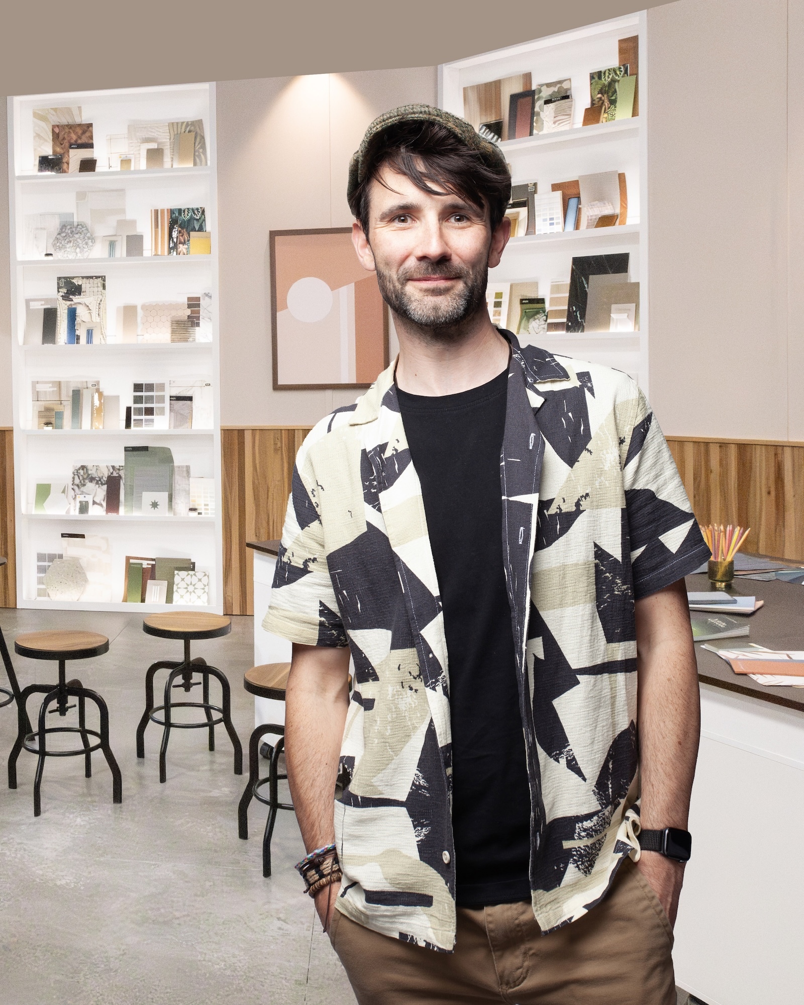 Portrait of J Cooper standing in modern office with white bookshelves and wooden stools.