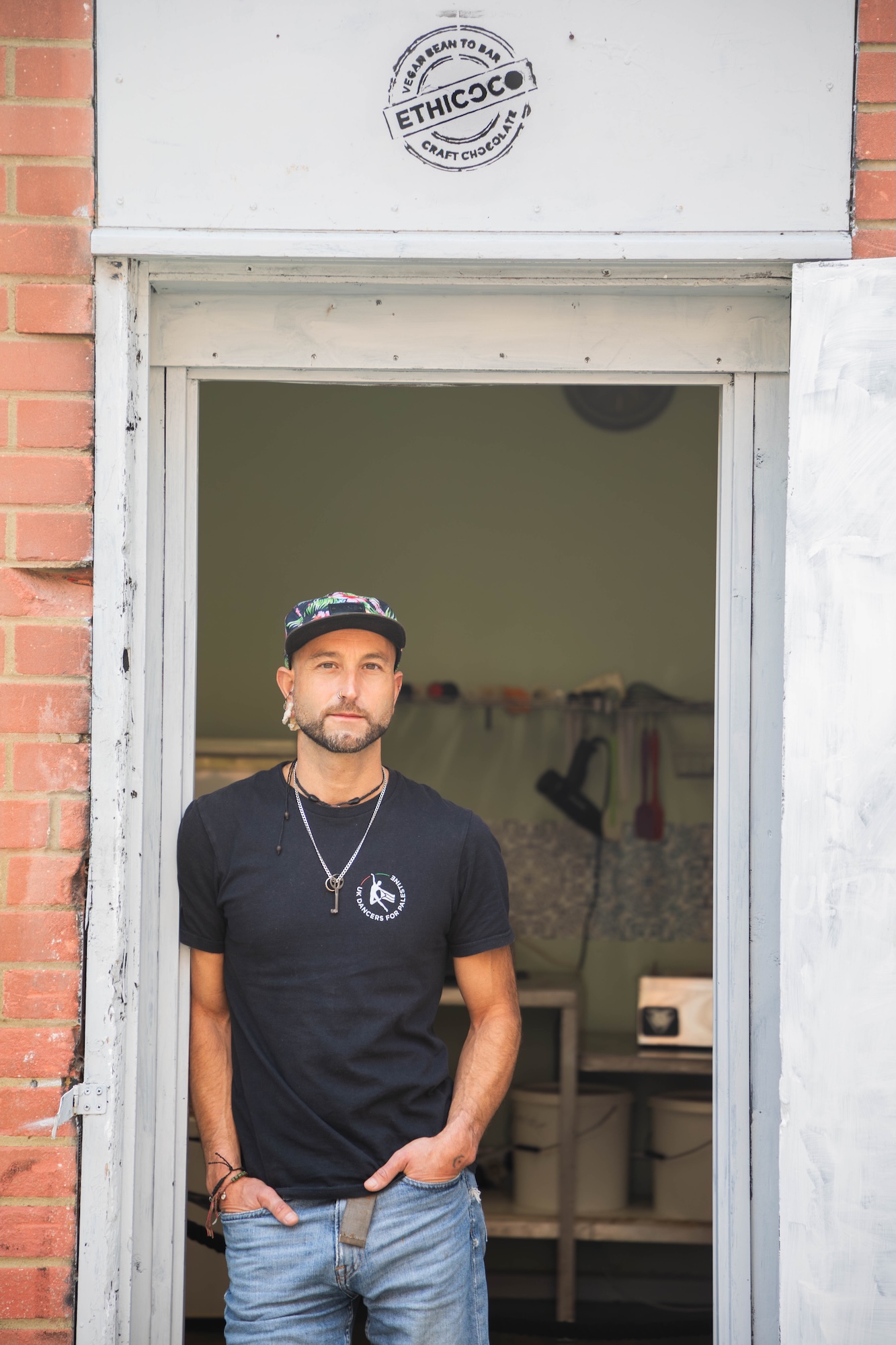 Portrait of J Tutton standing in the doorway of Ethicoco artisan chocolate and coffee shop in Boscombe, Bournemouth.