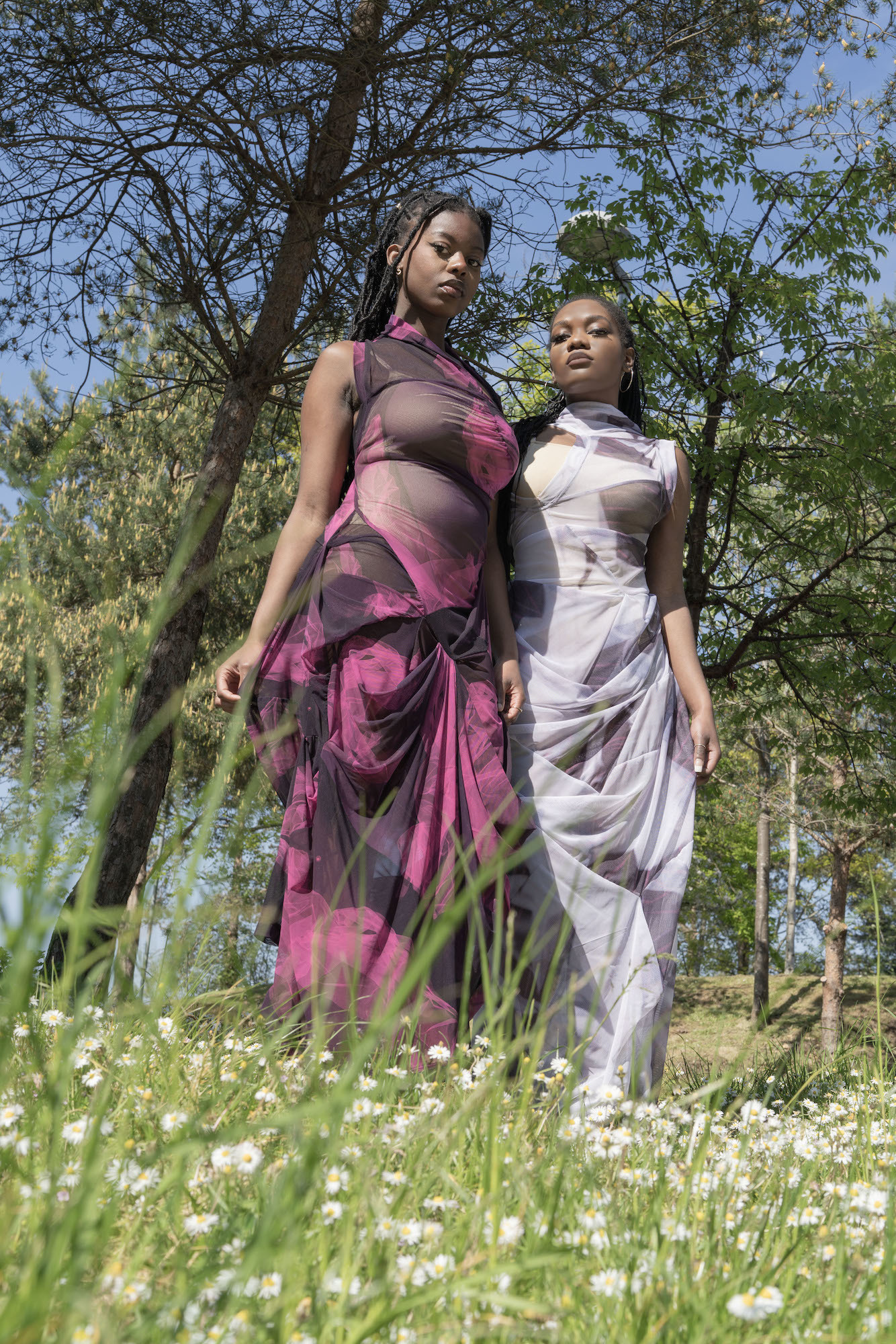 Two models modelling fashion gowns in a field.