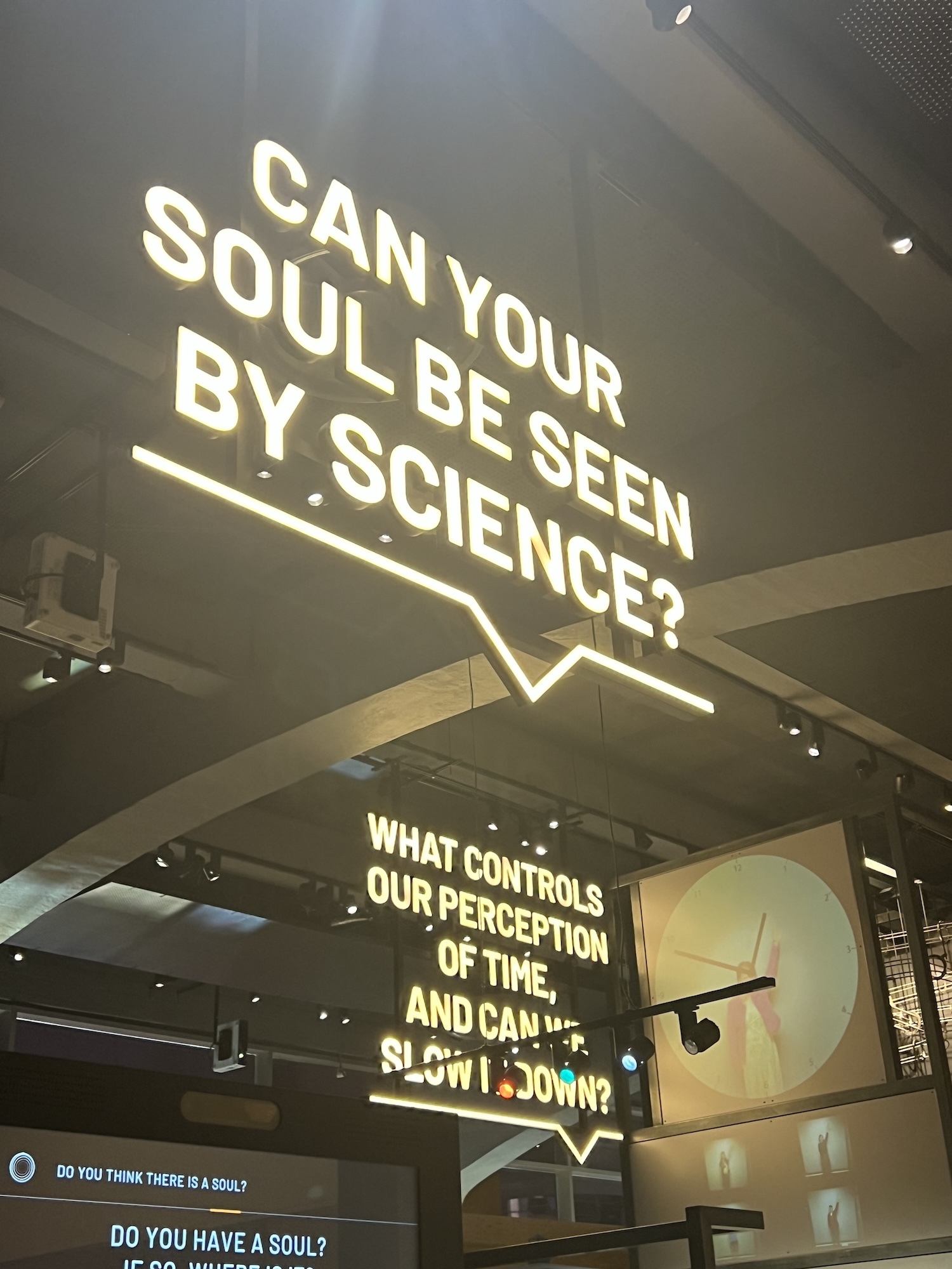 Museum display with large white text on ceiling asking "CAN YOUR SOUL BE SEEN BY SCIENCE?" with additional questions below in speech bubbles.