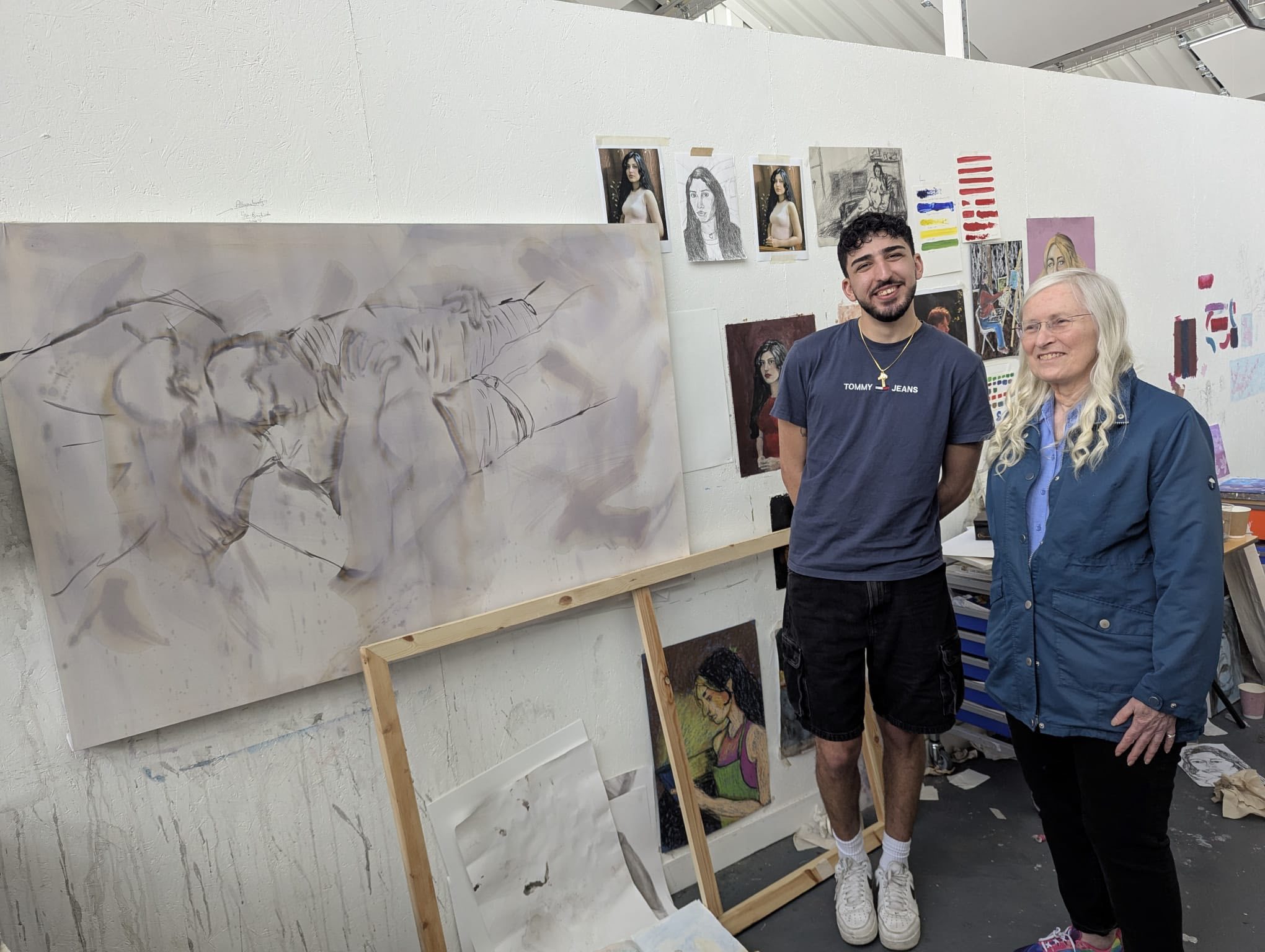 AUB Fine Art student and Julia stood in the fine art studio, to the left is a large canvas with faint, faded figures outlined.