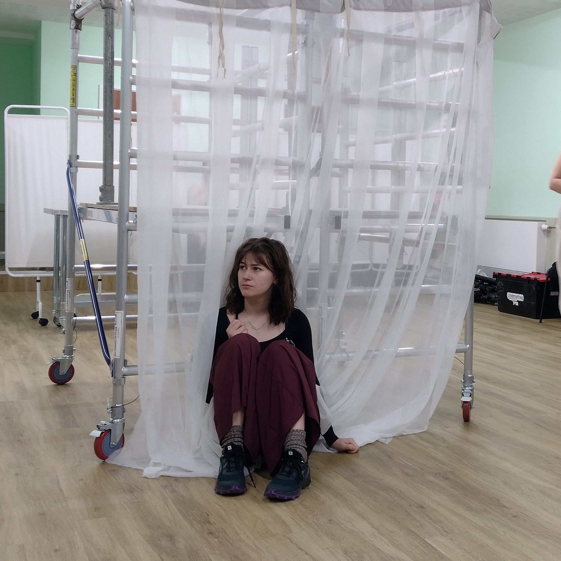 A BA (Hons) Acting student crouched next to a small scaffolding on wheels while rehearsing 'Romeo and Juliet'.