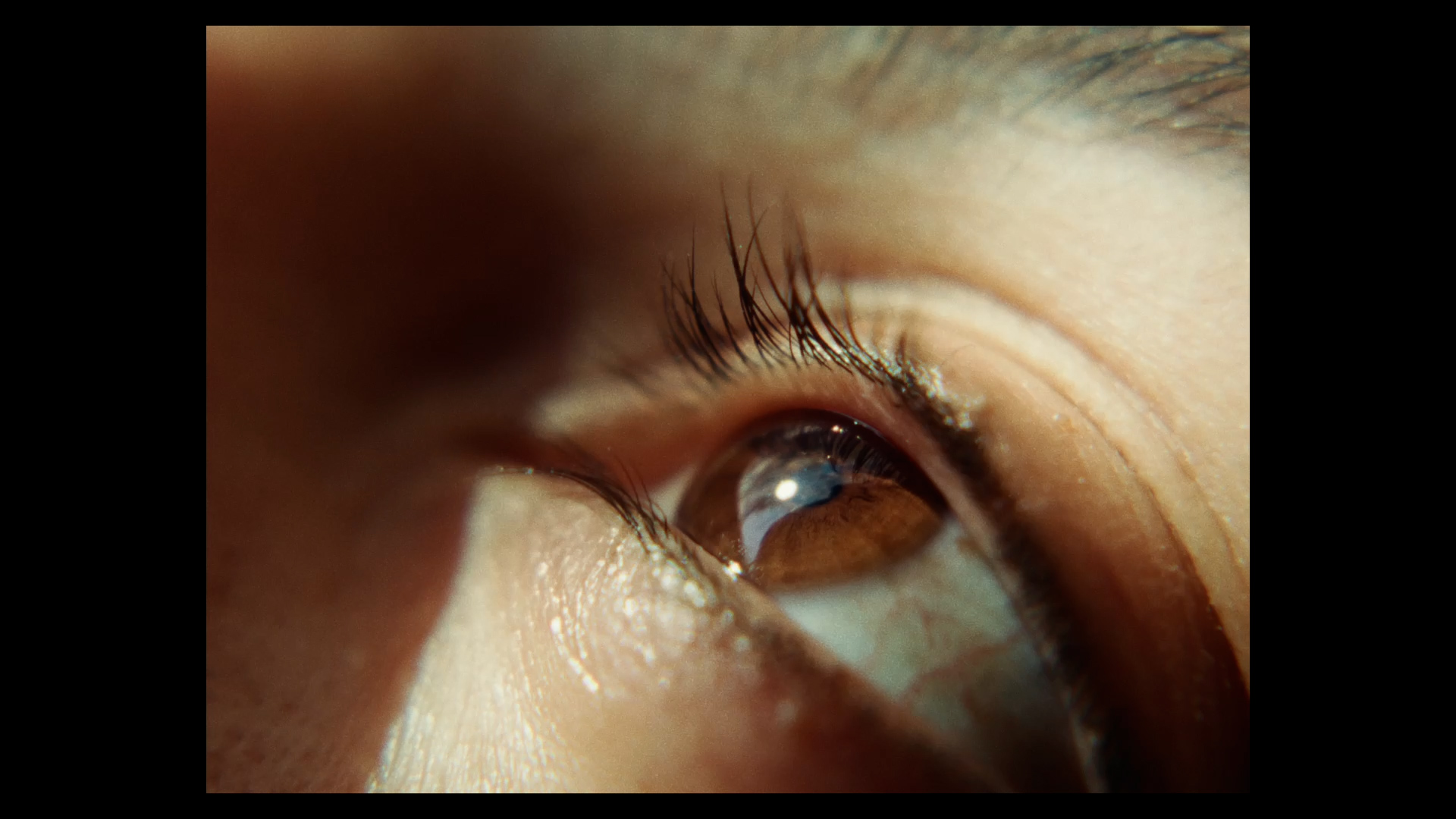 Close-up film still of a young person's eye looking up to the top left.
