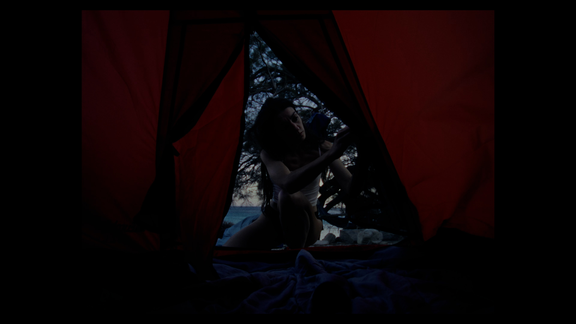 Film still of a woman entering a dark tent with red interior.