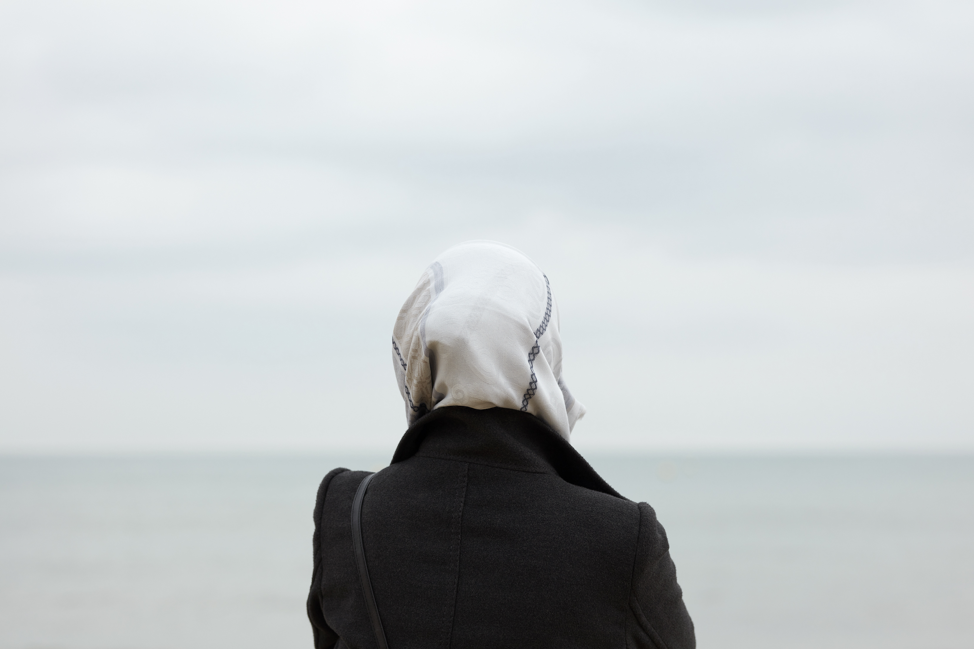 A person viewed from behind wearing a headscarf facing away from the camera looking out to sea.