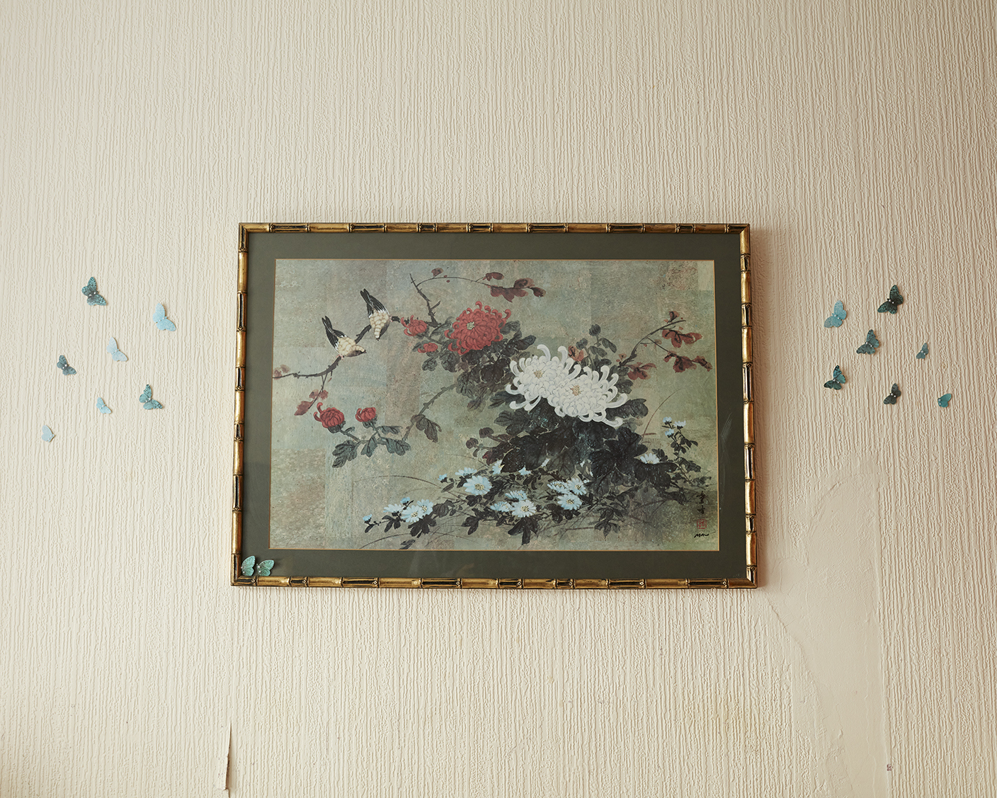 Framed painting flowers on a wall with butterflies decorated around it