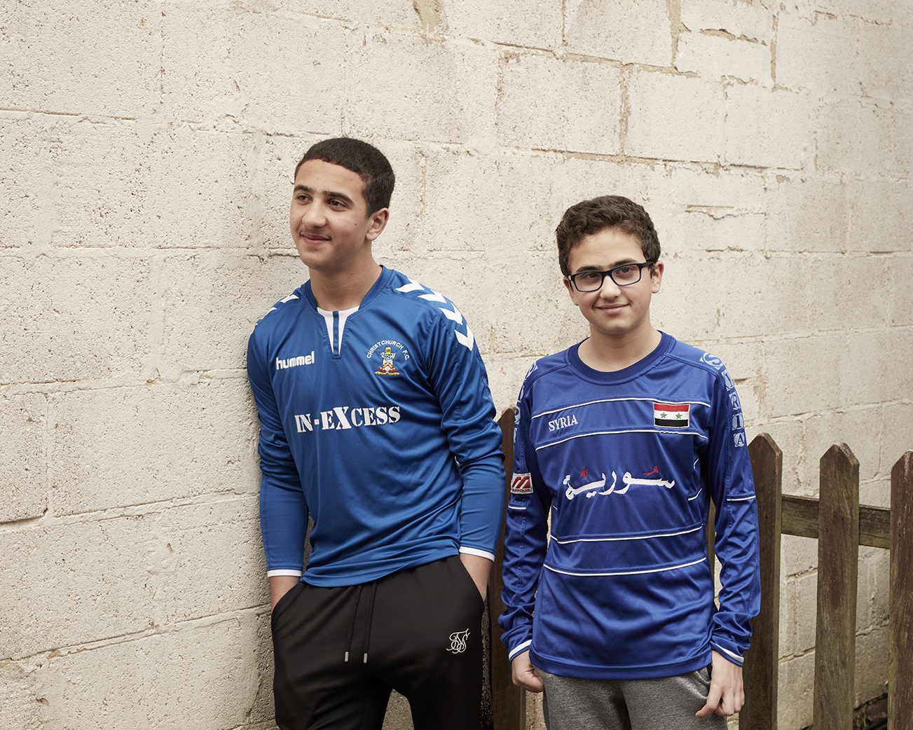 A pair of children in football shirts leaning against a wall, posing for the camera.