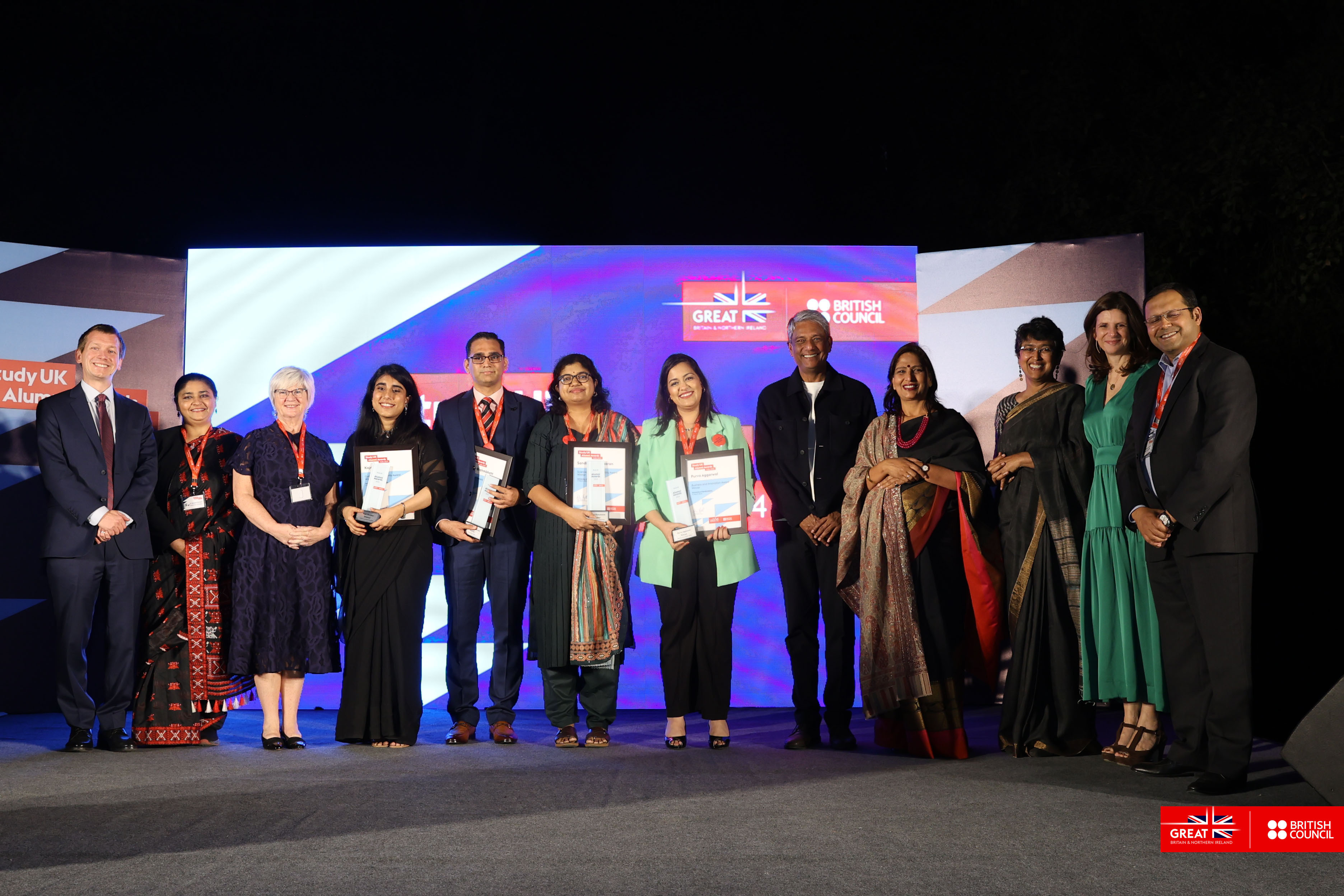 A group of award-winners and officials lined up to pose for a photo against a blue and white backdrop at the British Council Study UK Alumni Awards.