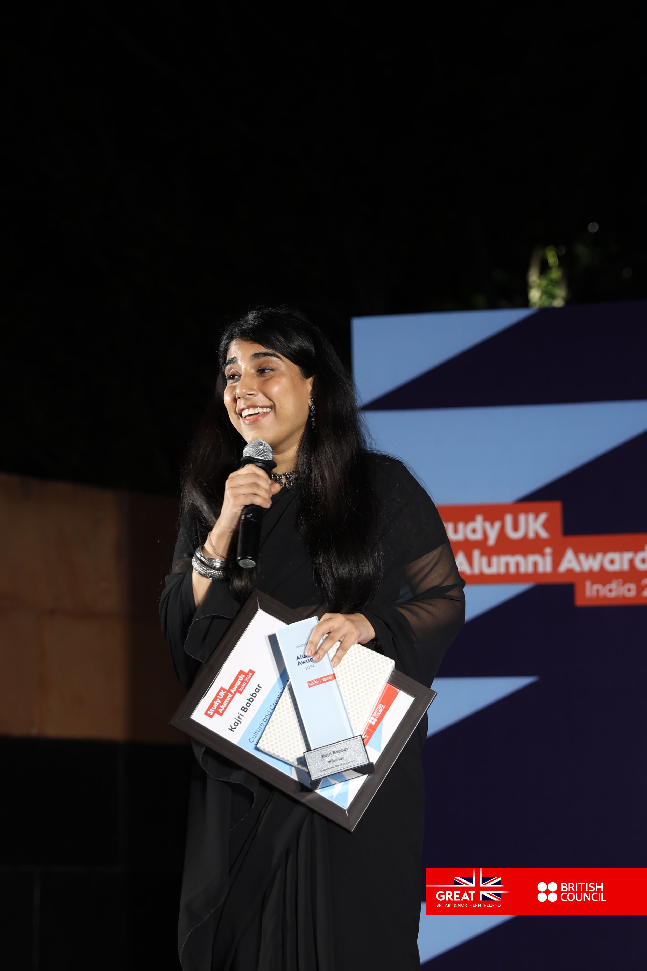K Babbar holding a microphone making a speech while accepting her award.