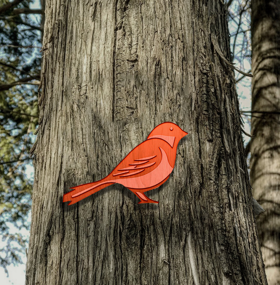 Orange paper bird cutout attached to brown tree trunk with textured bark, bare branches visible in background.