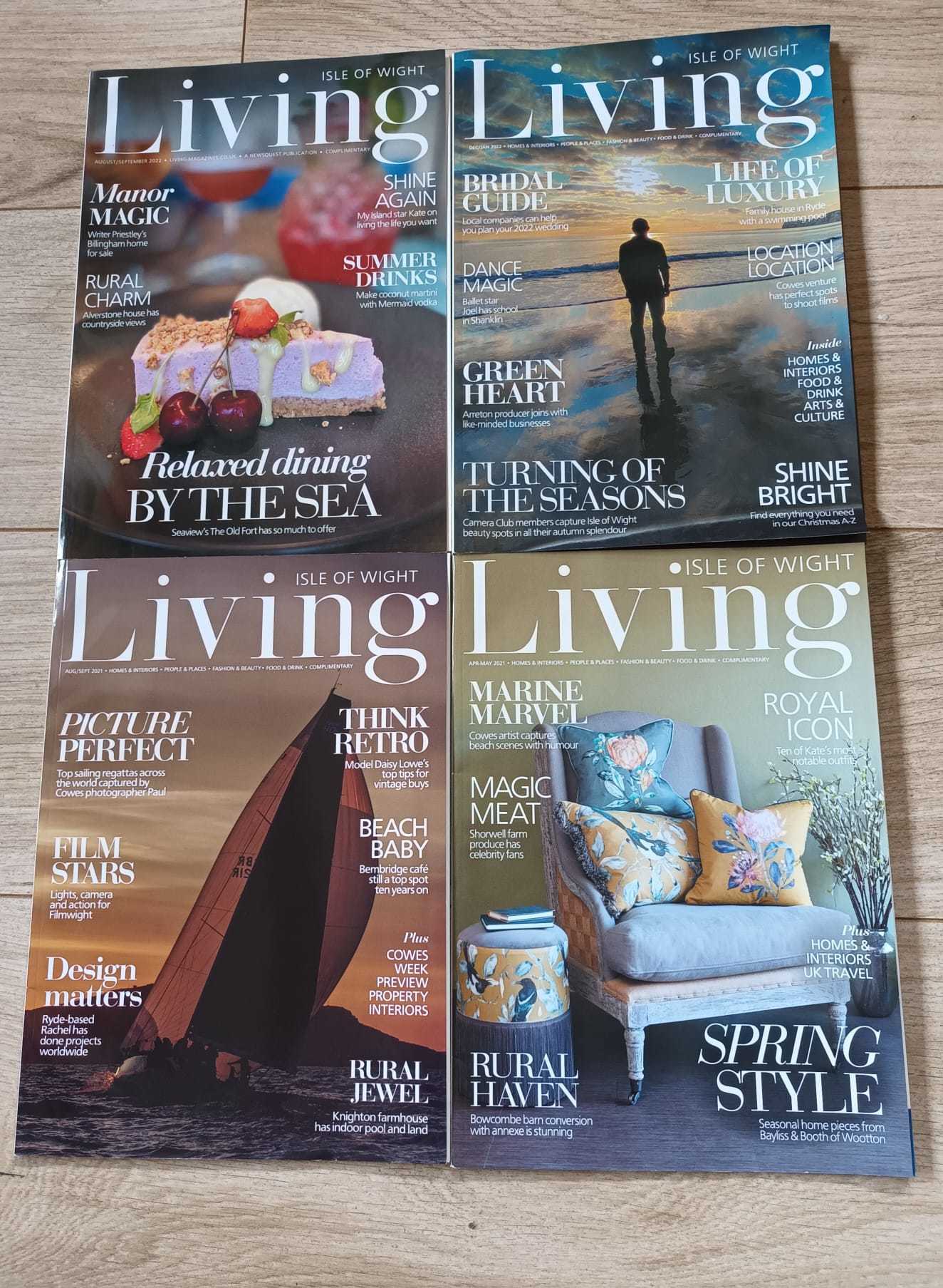 Four issues of Isle of Wight Living magazine, arranged in a grid formation and on display on a wooden background.
