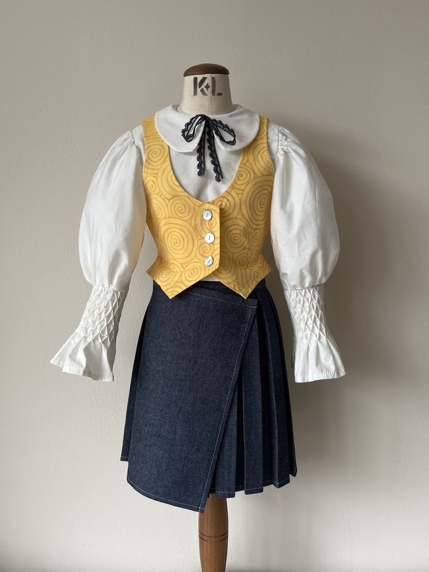 Traditional costume on mannequin: white blouse with puffy sleeves, yellow patterned waistcoat, navy wrap skirt, black neck ribbon.