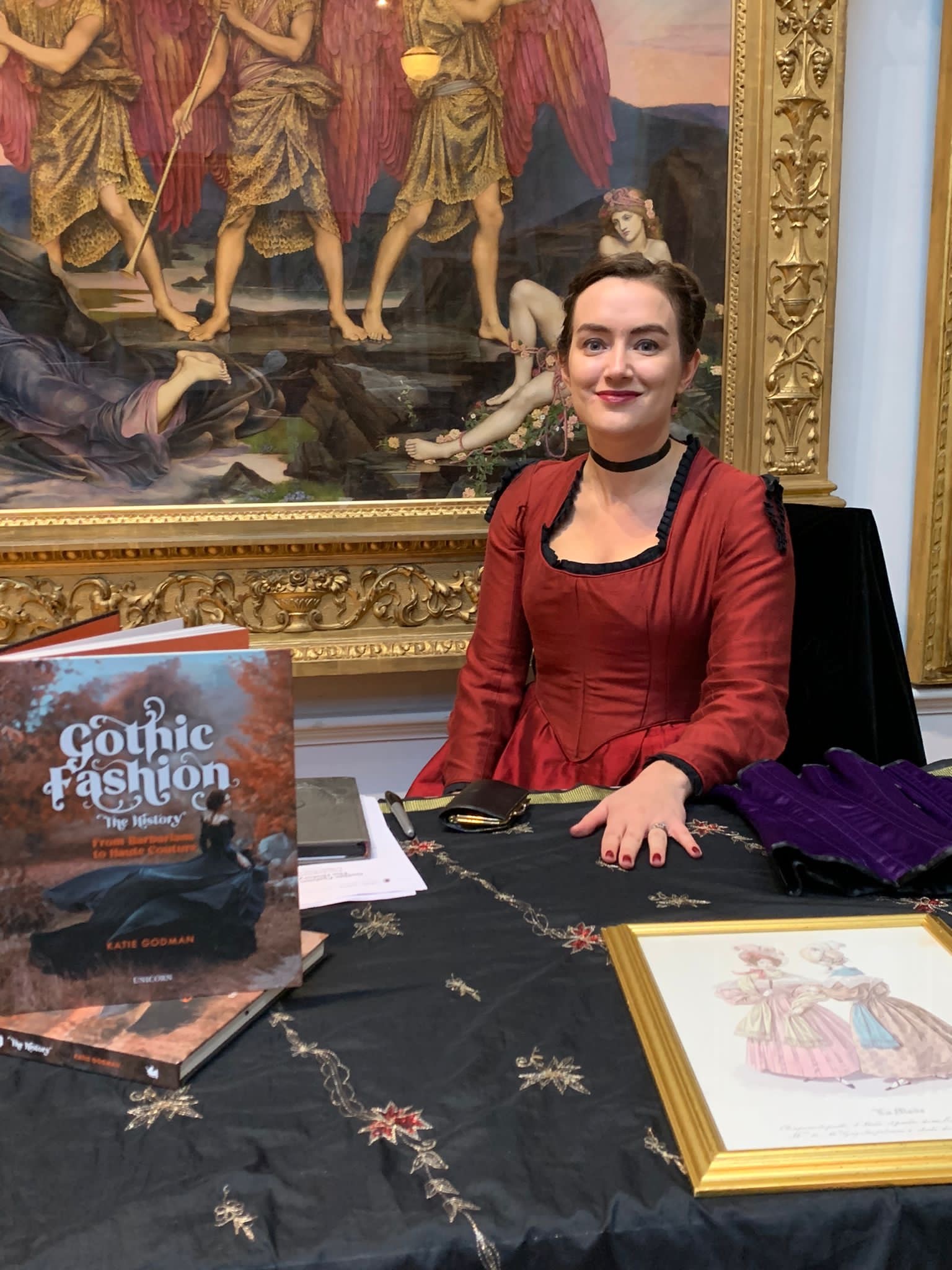 Portrait of K Godman sitting at a table with a copy of Gothic Fashion: The History next to her.