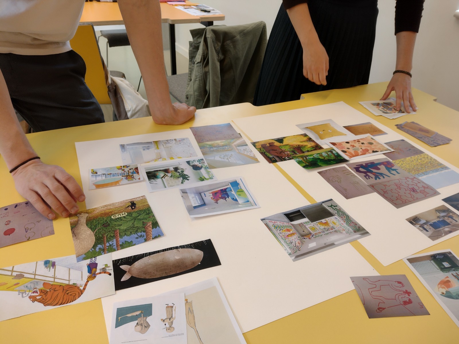 Two people leaning over a table and arranging pictures to make a collage.