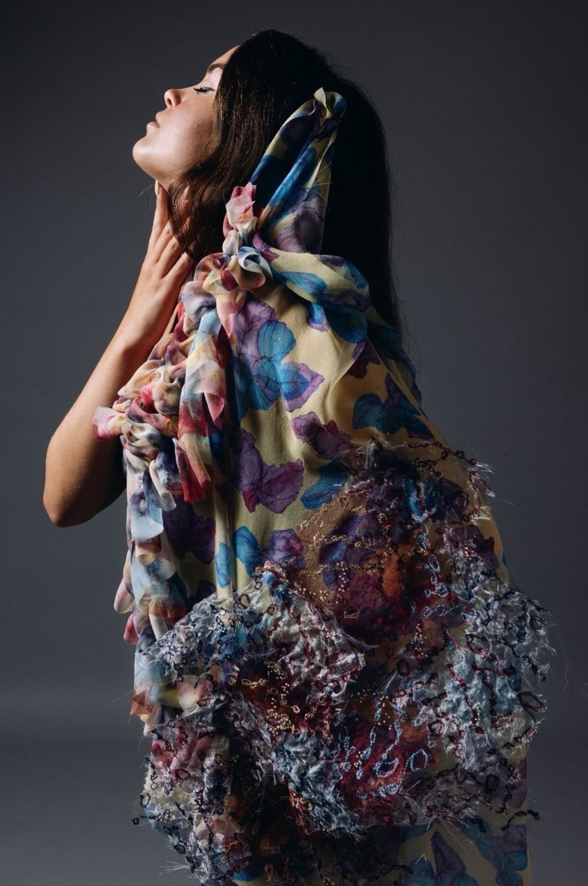 Model wearing layered fabrics, blue, yellow and brown, grey background.