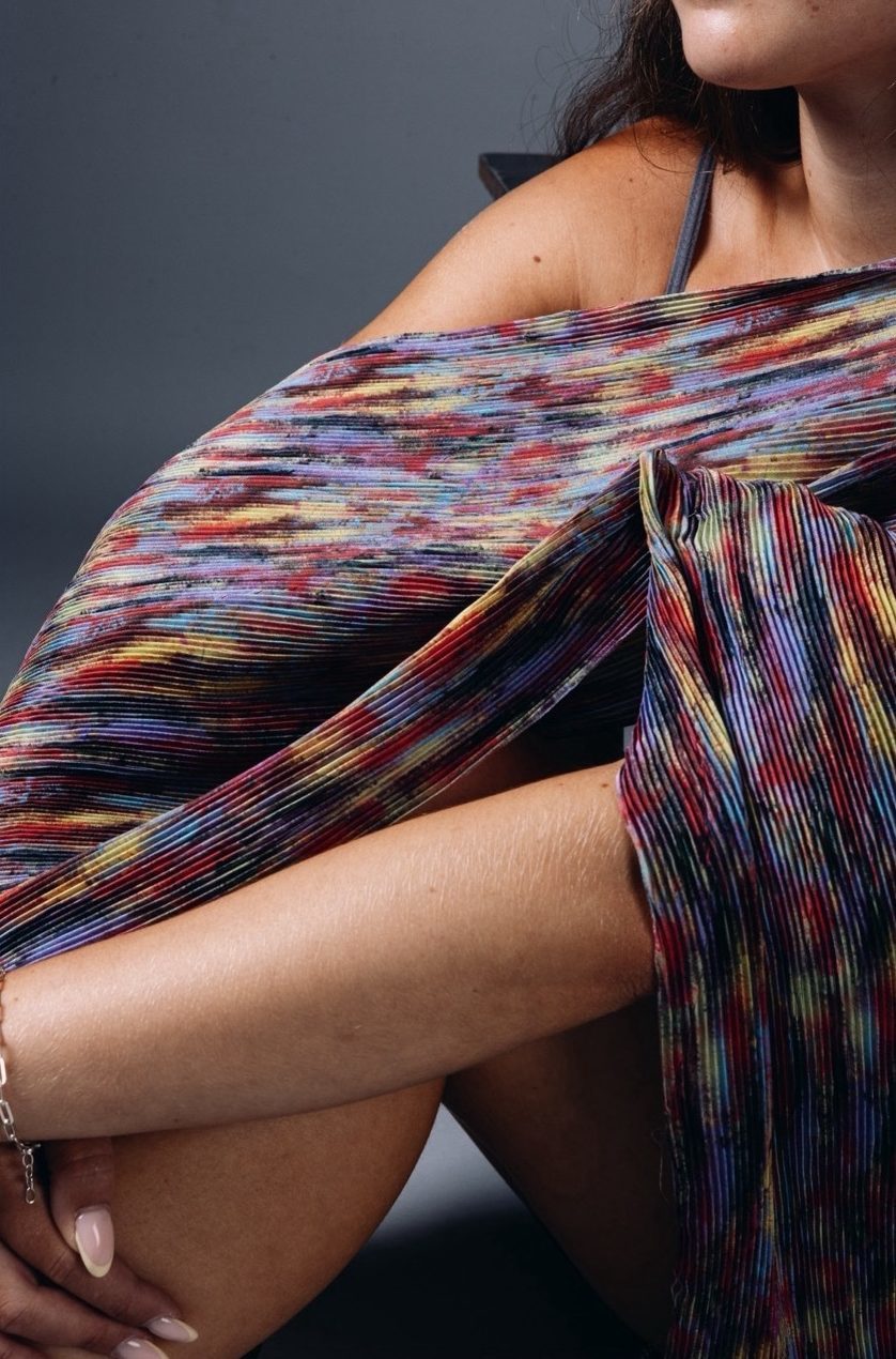 Model wearing a fabric dress piece, red, yellow and blue, grey background.