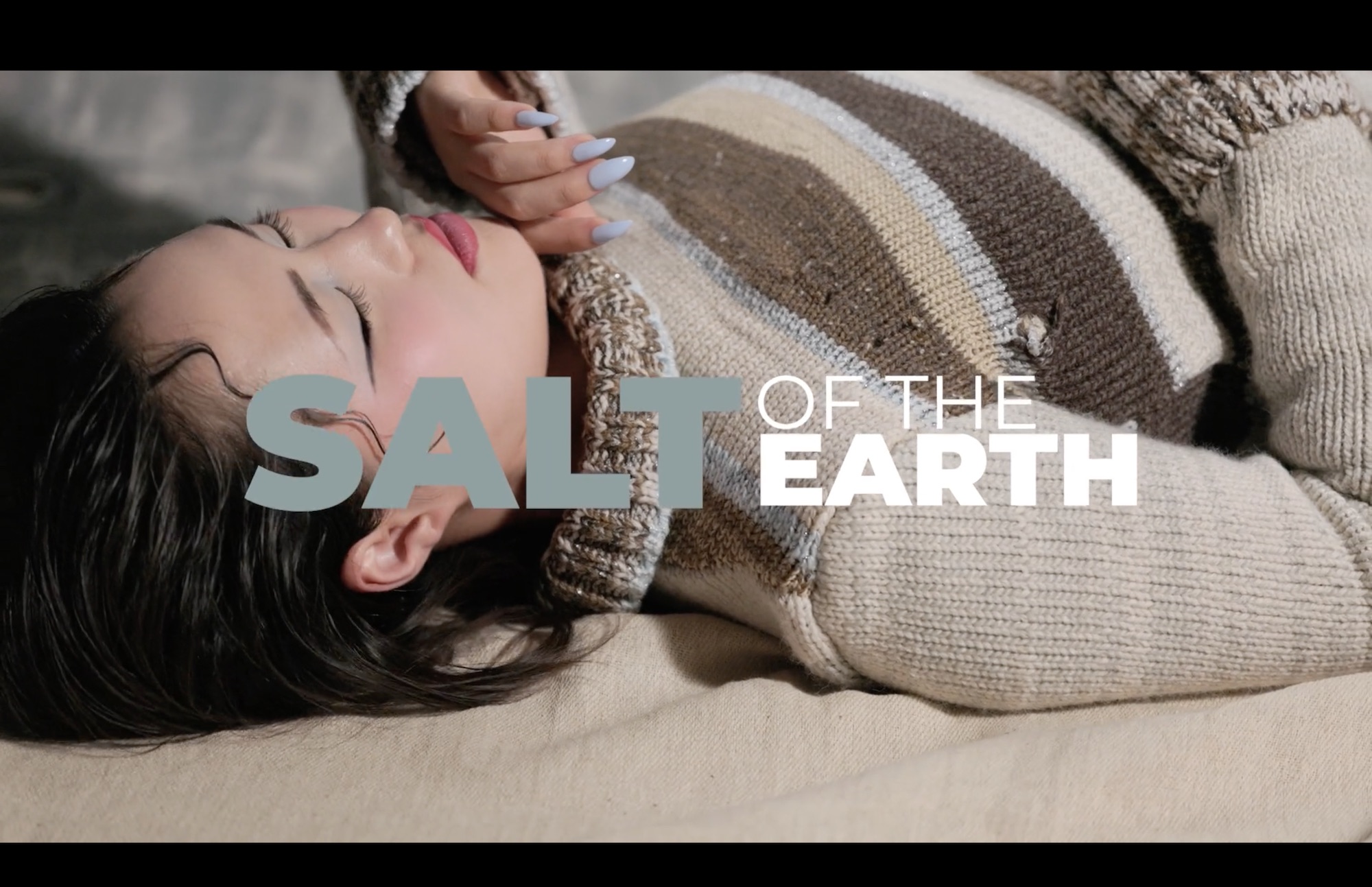 A woman lying on a sofa wearing a beige knitted jumper and striped sweater, with the words "Salt of the Earth" overlaid across the image.