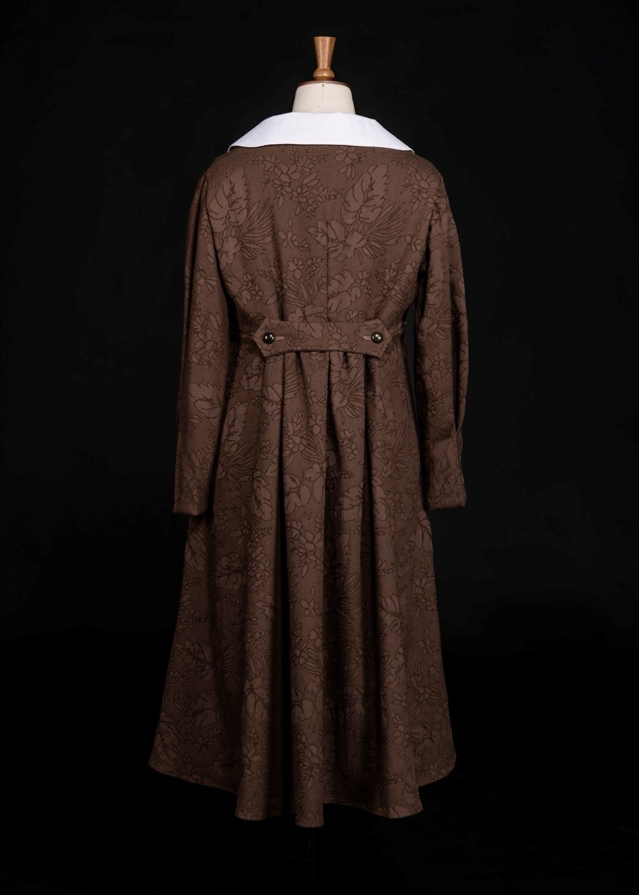 Brown patterned coat with white collar displayed on dress form, rear view showing back belt detail against black background.