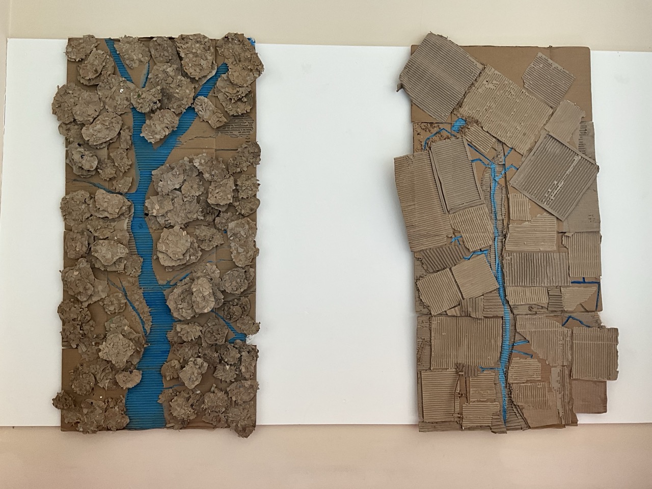 Two textured cardboard relief panels on a white board, one made of rough brown clumps and the other of layered corrugated pieces, both split by a blue vertical line.