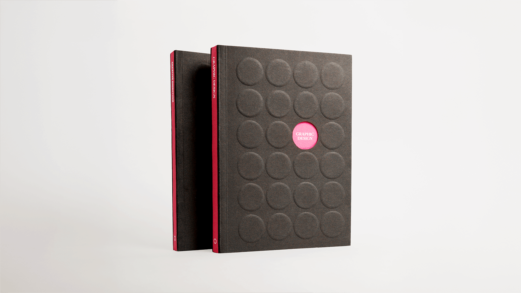 Black notebook with embossed circular grid pattern and pink trim, standing upright against white background.