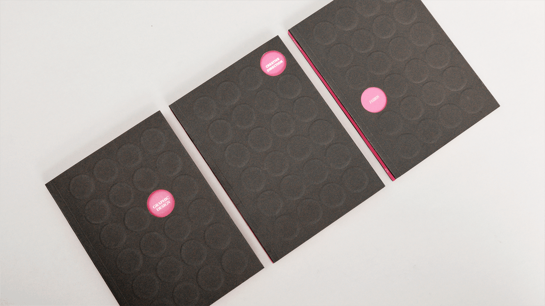 Three dark grey rectangular cards arranged in a row on white surface, each containing pink circular elements, middle card has pink stripe.