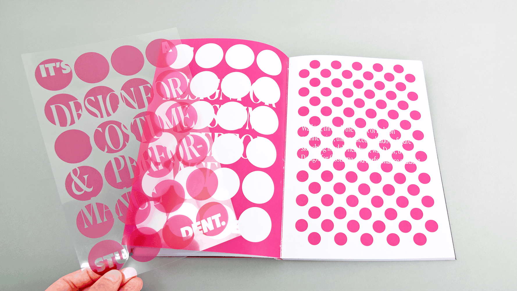 Open book with pink and white circular patterns on both pages, hand holding bottom corner, white background.