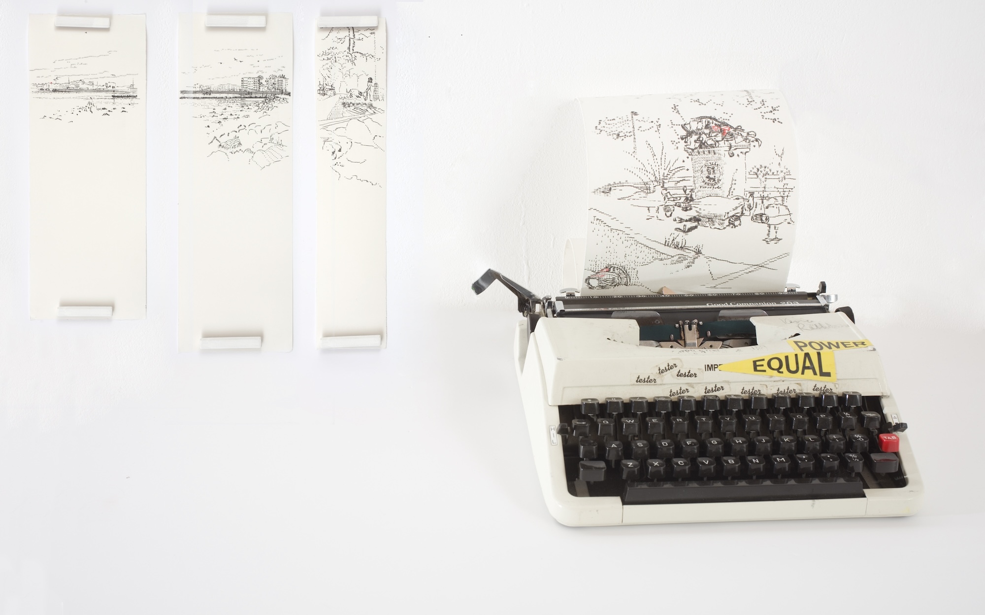 Three strips of long paper with small landscape pictures on each. A typewriter is next to them, with another piece of paper with a drawing on it loading into the typewriter.