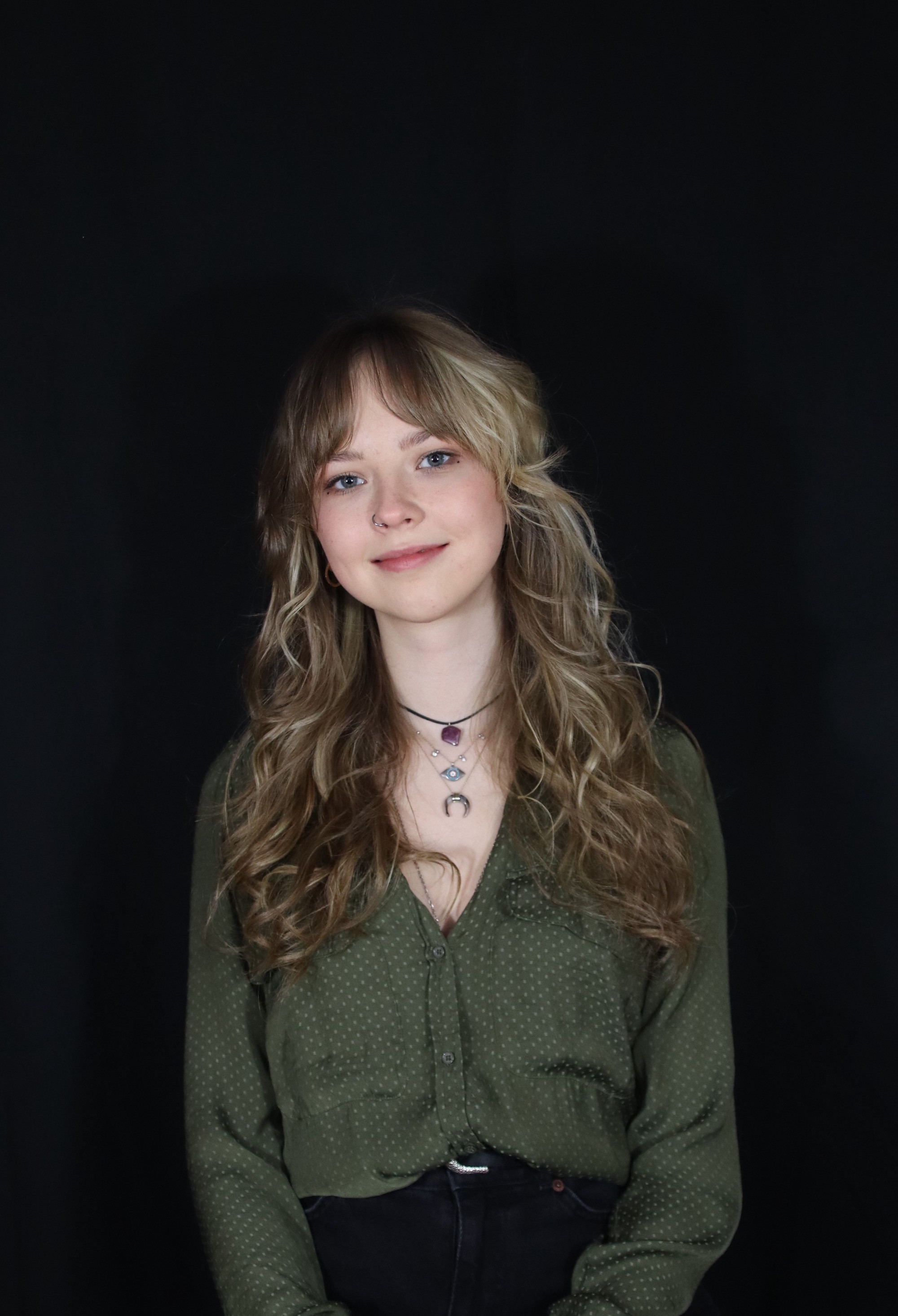A person stands smiling, facing the camera against a dark background