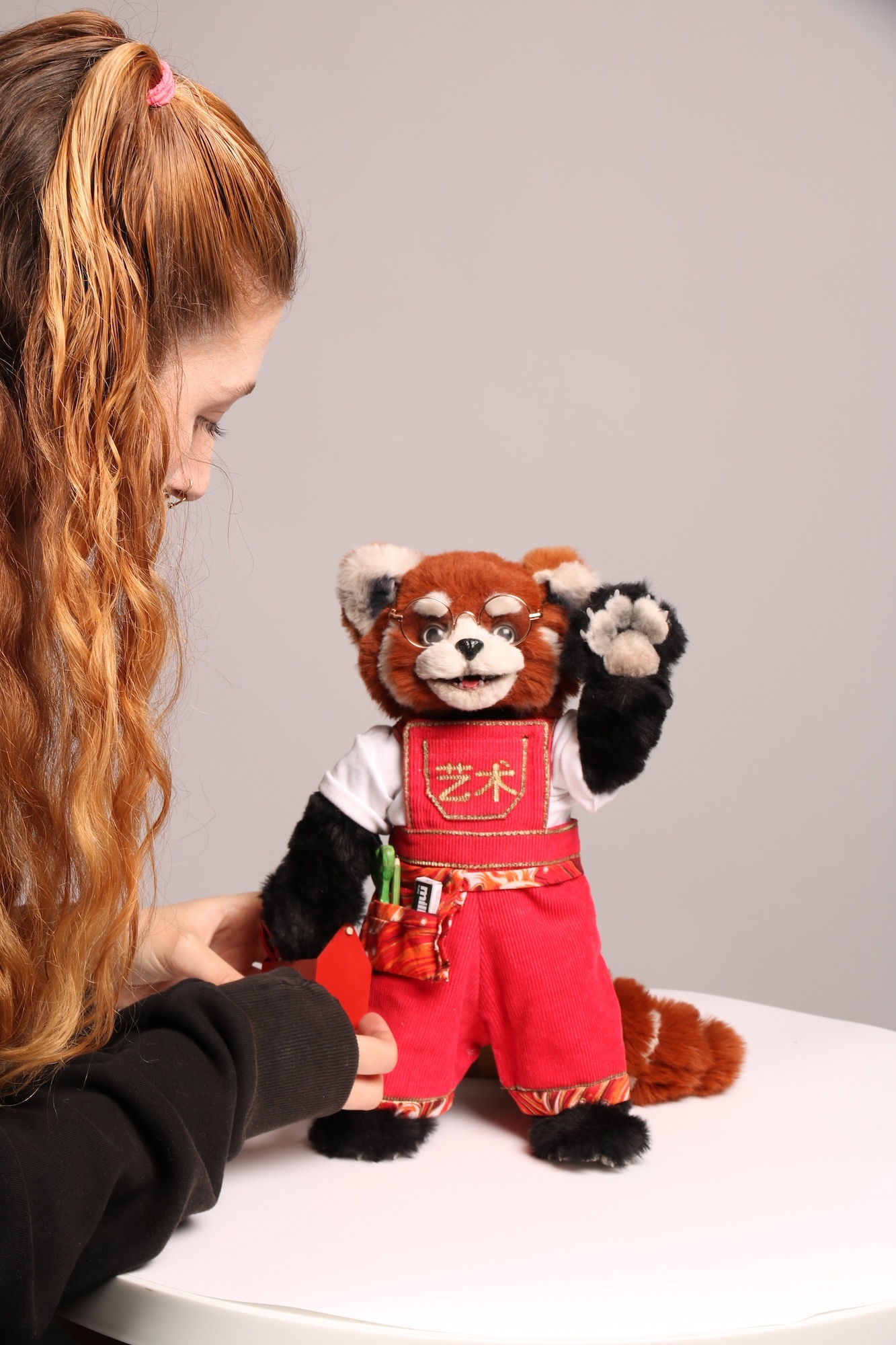 A BA (Hons) Modelmaking student with a puppet of a red panda wearing a red and white outfit.